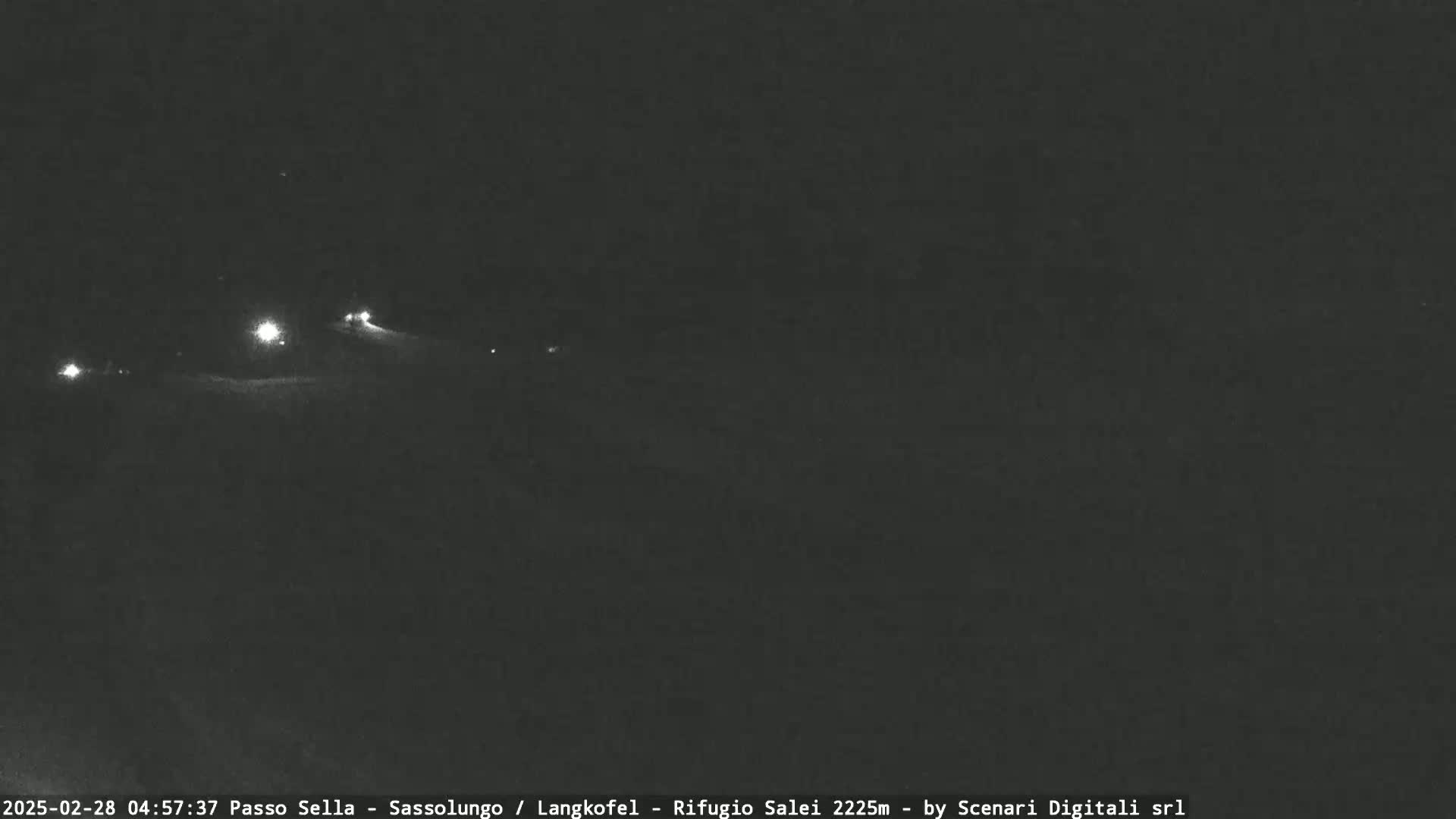 At night, several small lights are visible in the distance on a dark, snow-covered landscape.