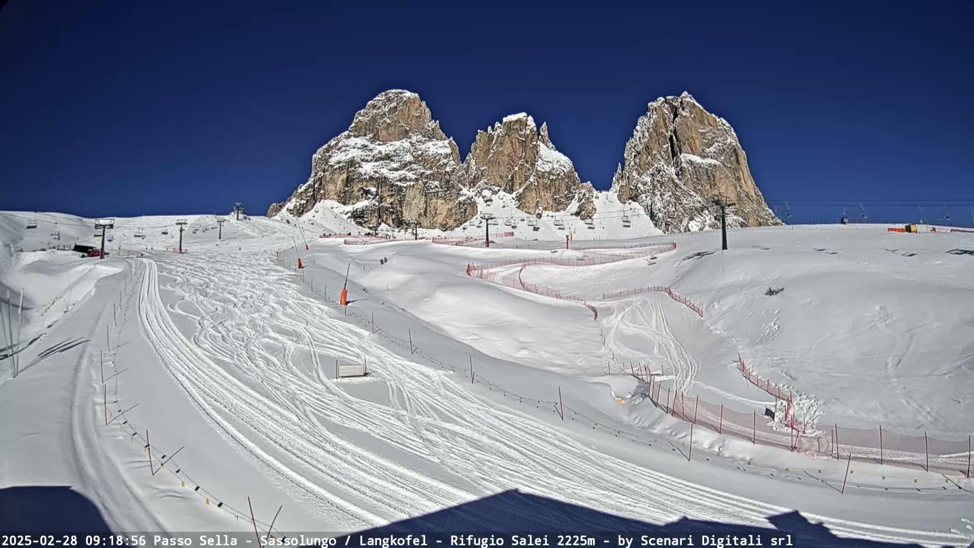 A snow-covered ski slope with ski lifts and three prominent rock formations in the background under a clear blue sky.