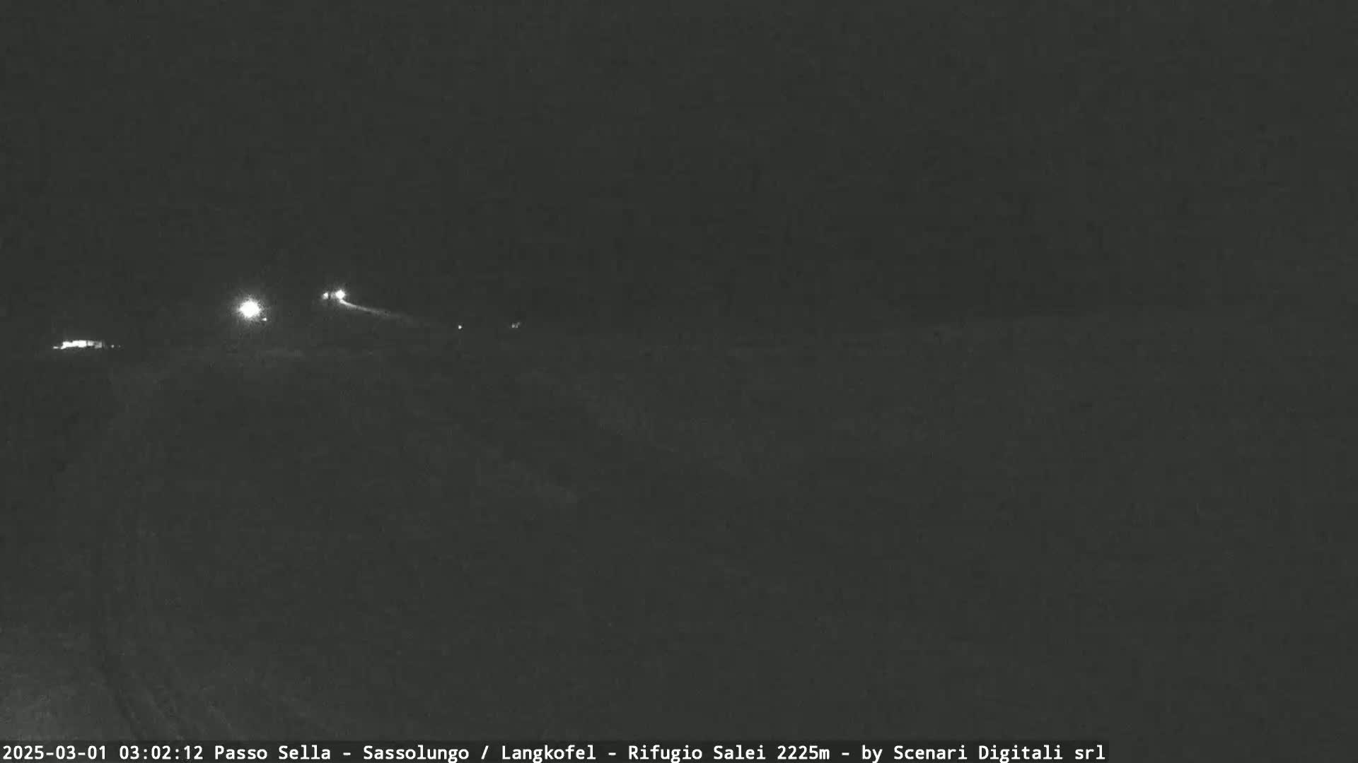 A dark, nighttime scene shows a road with a few faint lights in the distance.