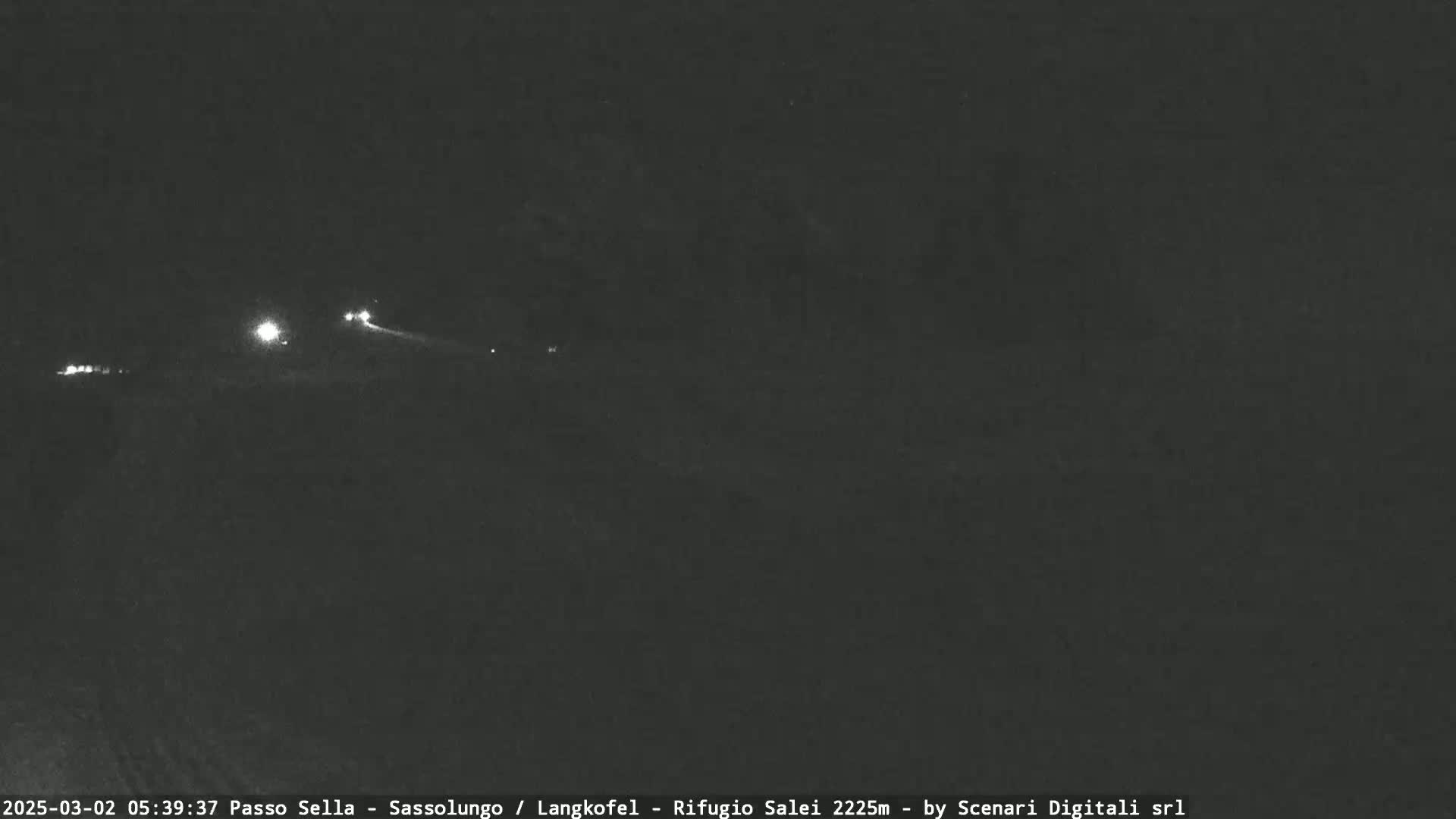 At night, several small lights are visible in the distance on a dark road.