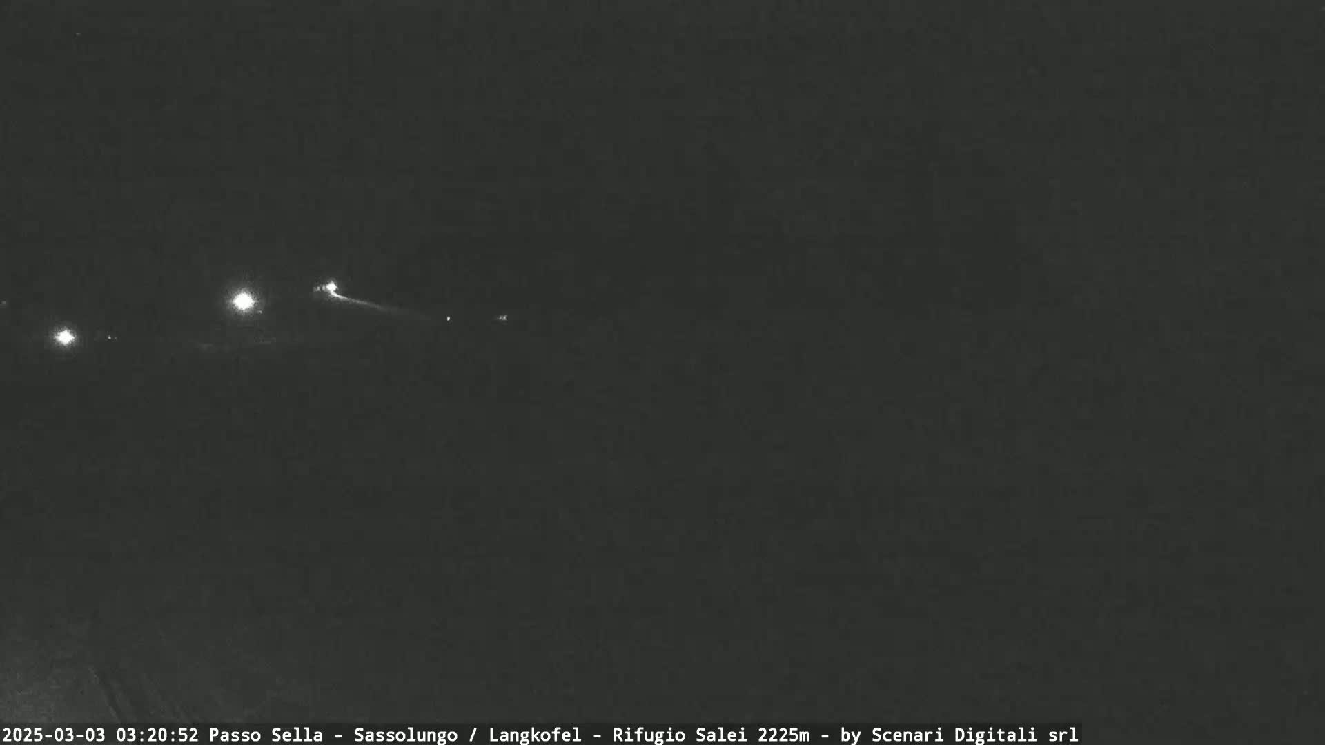 A nighttime long shot of a dark road with a few distant headlights visible.