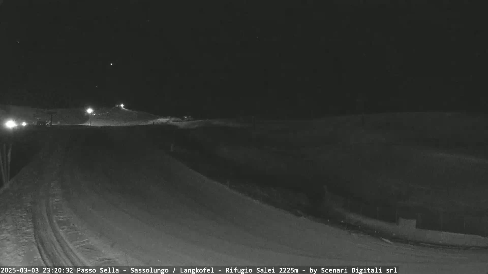 A snow-covered, gently sloping landscape is visible at night, illuminated by a few distant lights.