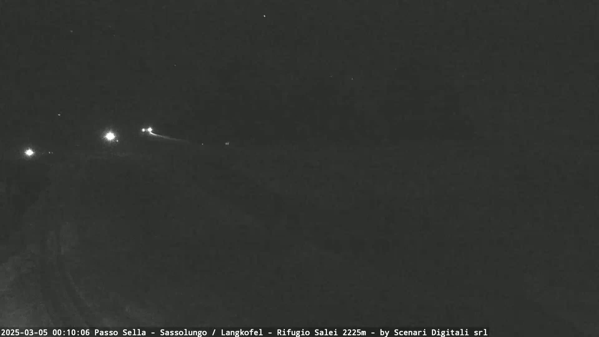 A nighttime long shot shows a dark landscape with a few distant lights visible under a clear, starry sky.