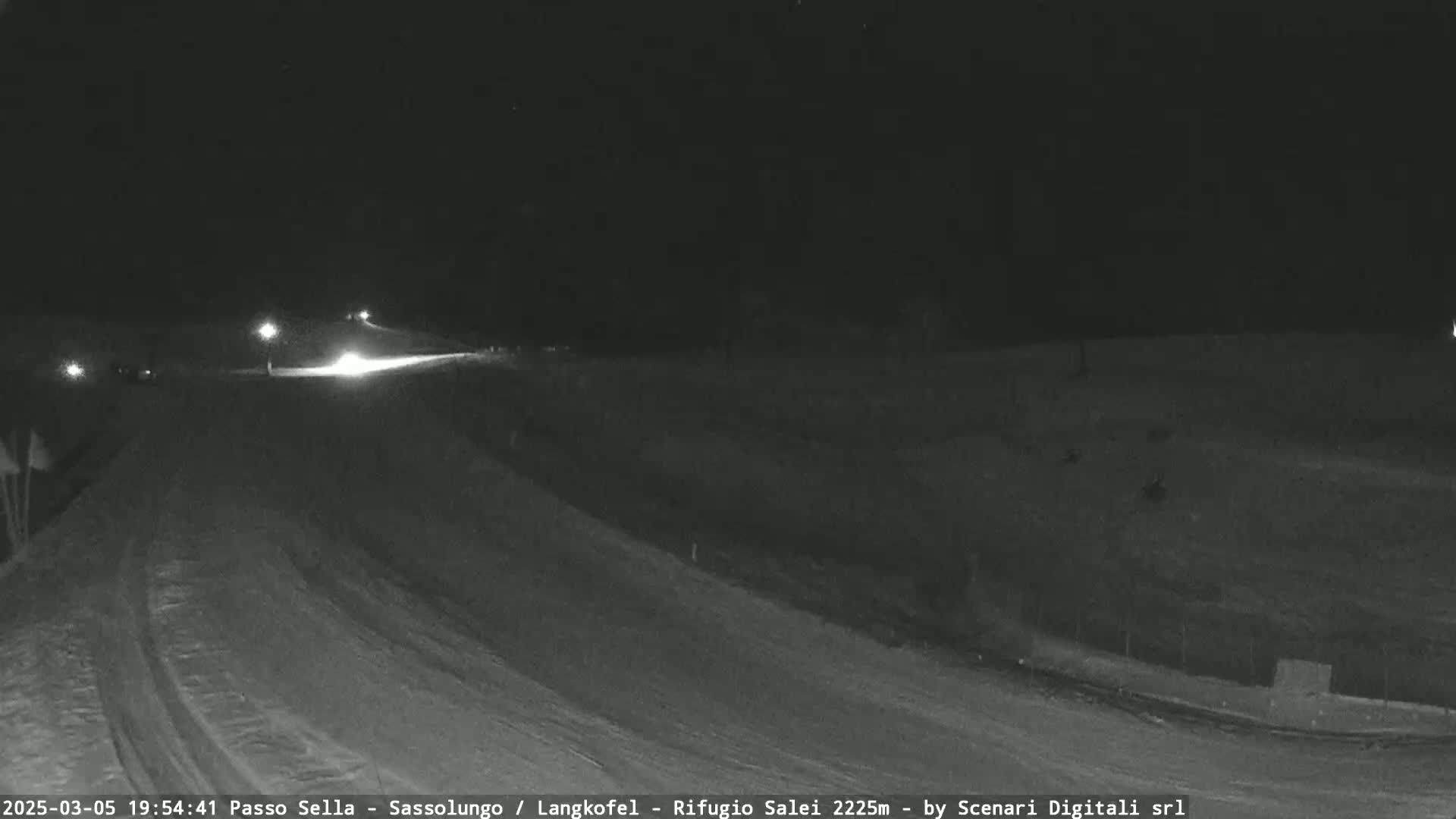 A snow-covered road at night with a few vehicles driving on it, under dark, clear skies.