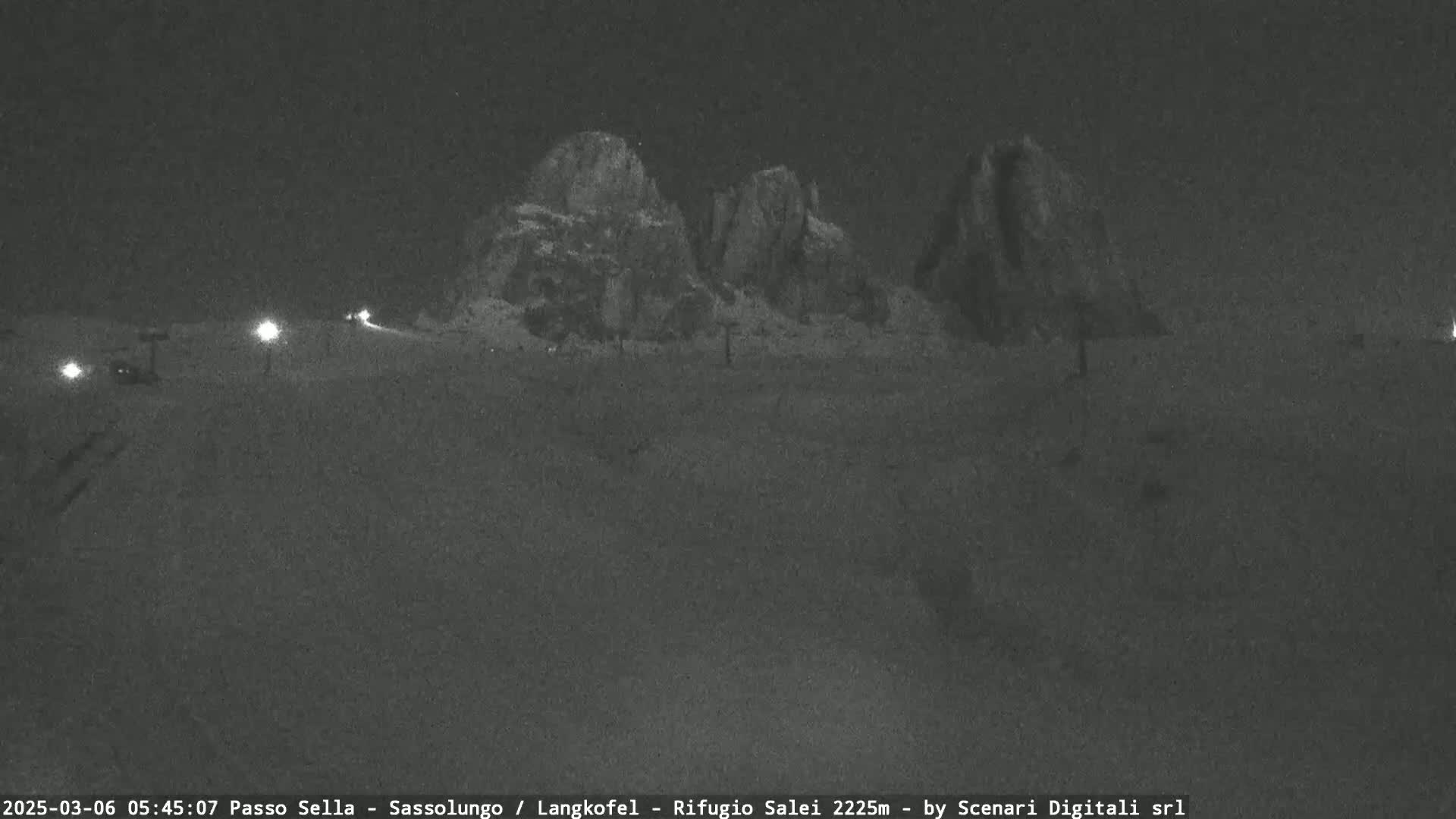 A nighttime, snow-covered landscape shows several large, dark rock formations under a clear sky, with a road visible in the foreground.