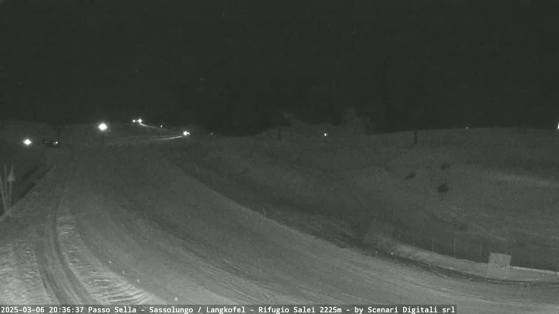 A nighttime, snow-covered road with a few vehicles visible under dark skies.