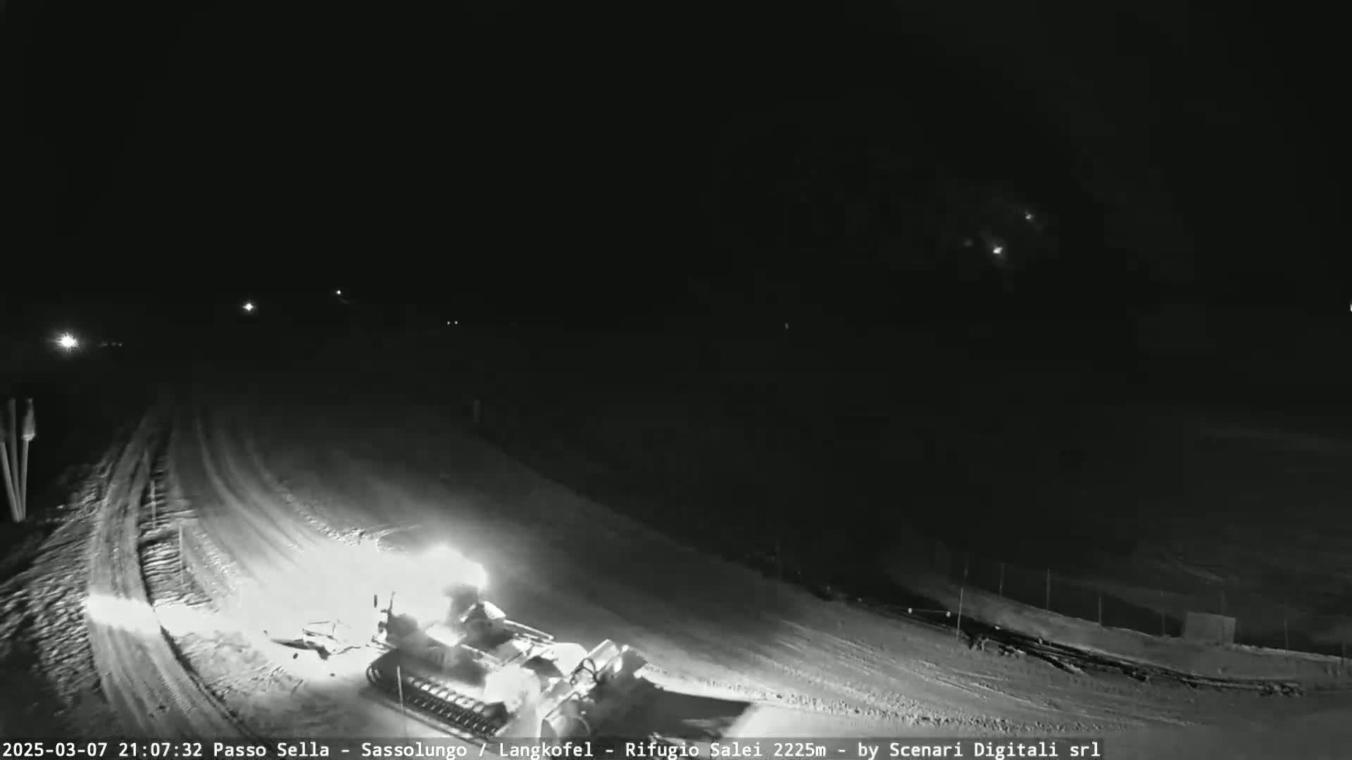 A snow groomer is working on a snow-covered road at night.