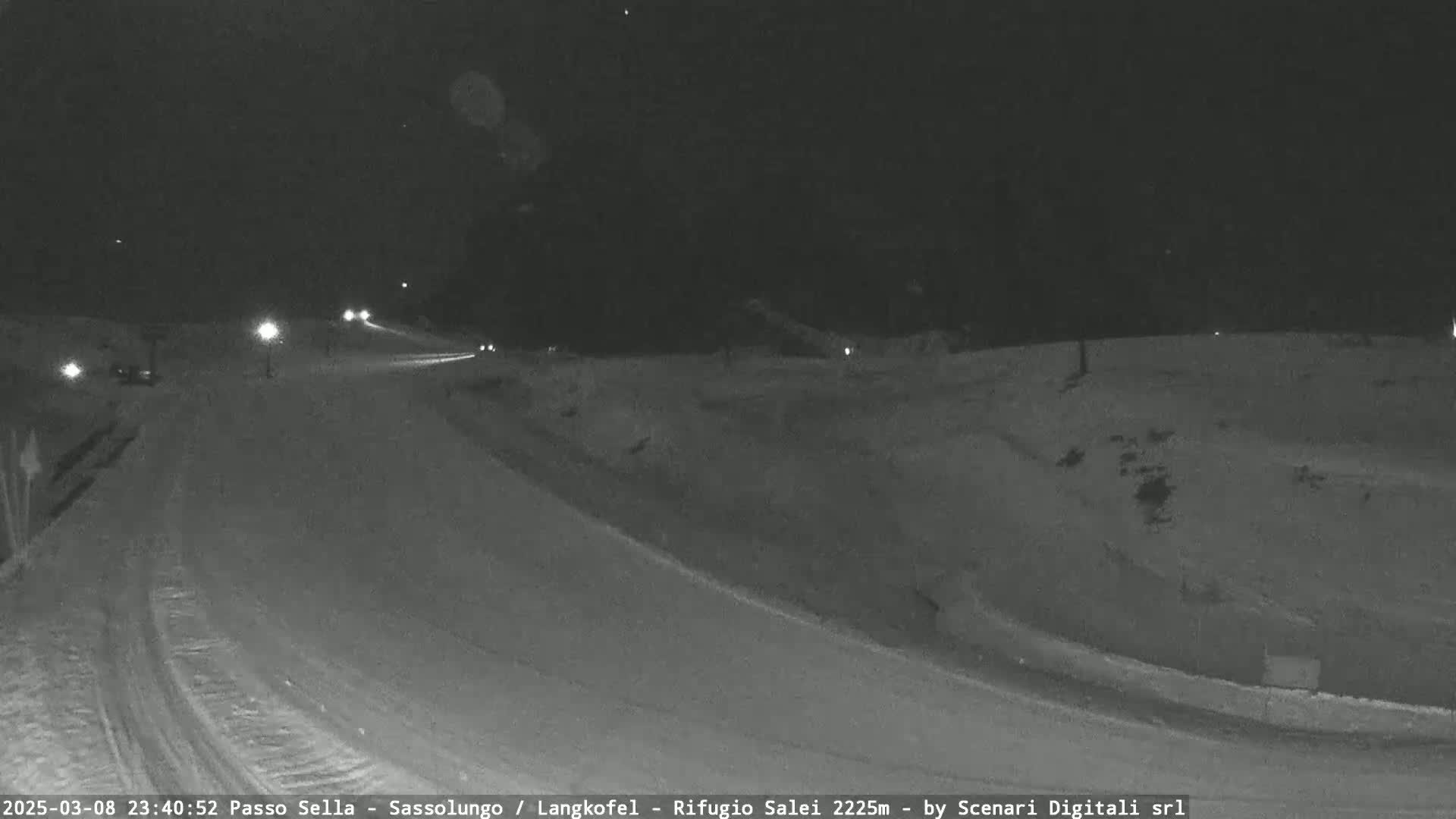 A snow-covered road at night with a few vehicles visible under dim lighting.
