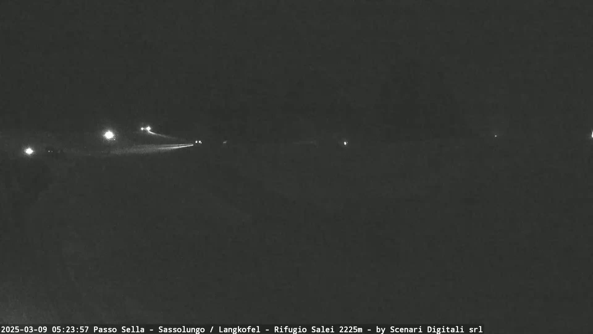 Headlights from several vehicles are visible on a dark road at night.