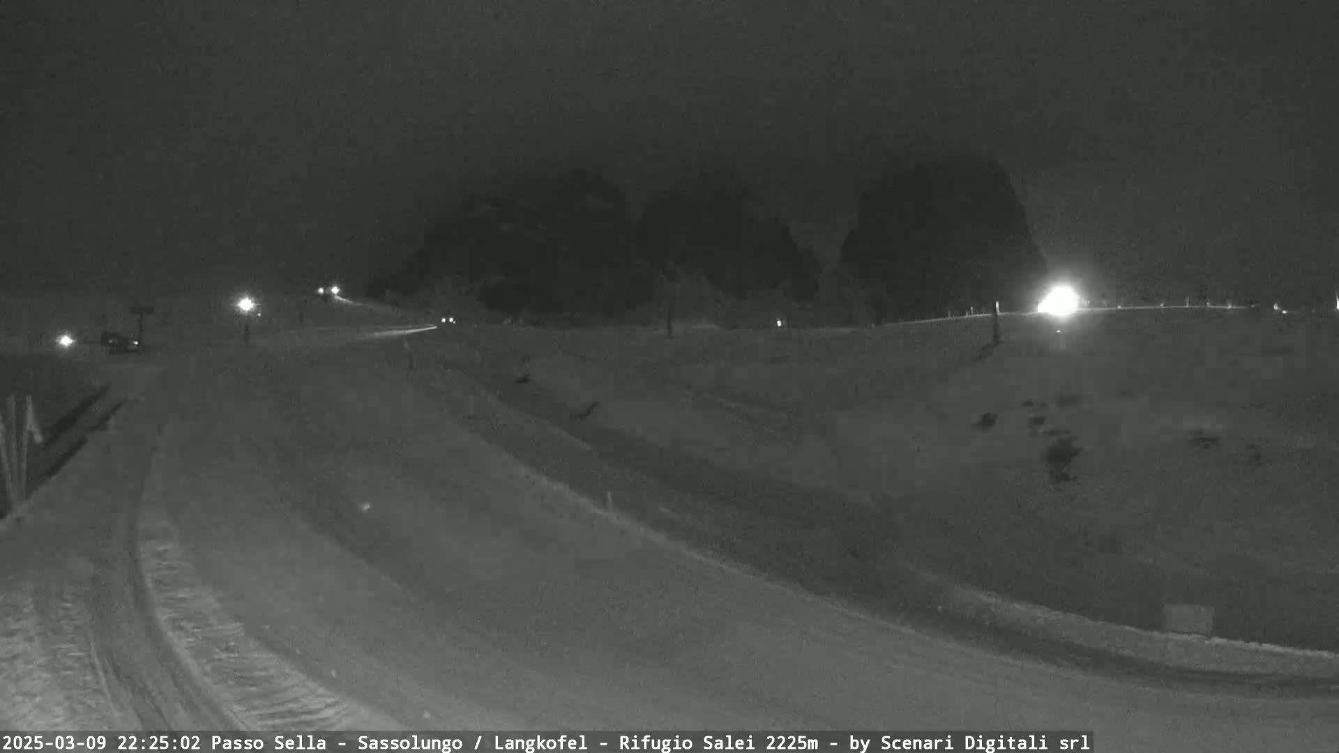A snow-covered road winds through a mountainous landscape at night, illuminated by sparse lighting.