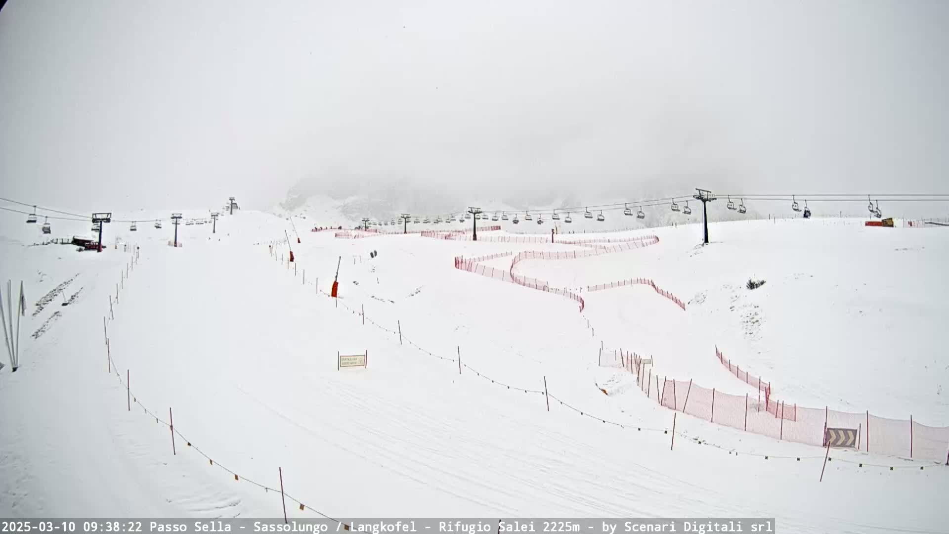 A snow-covered ski slope with several chairlifts and red safety nets is visible in foggy conditions.