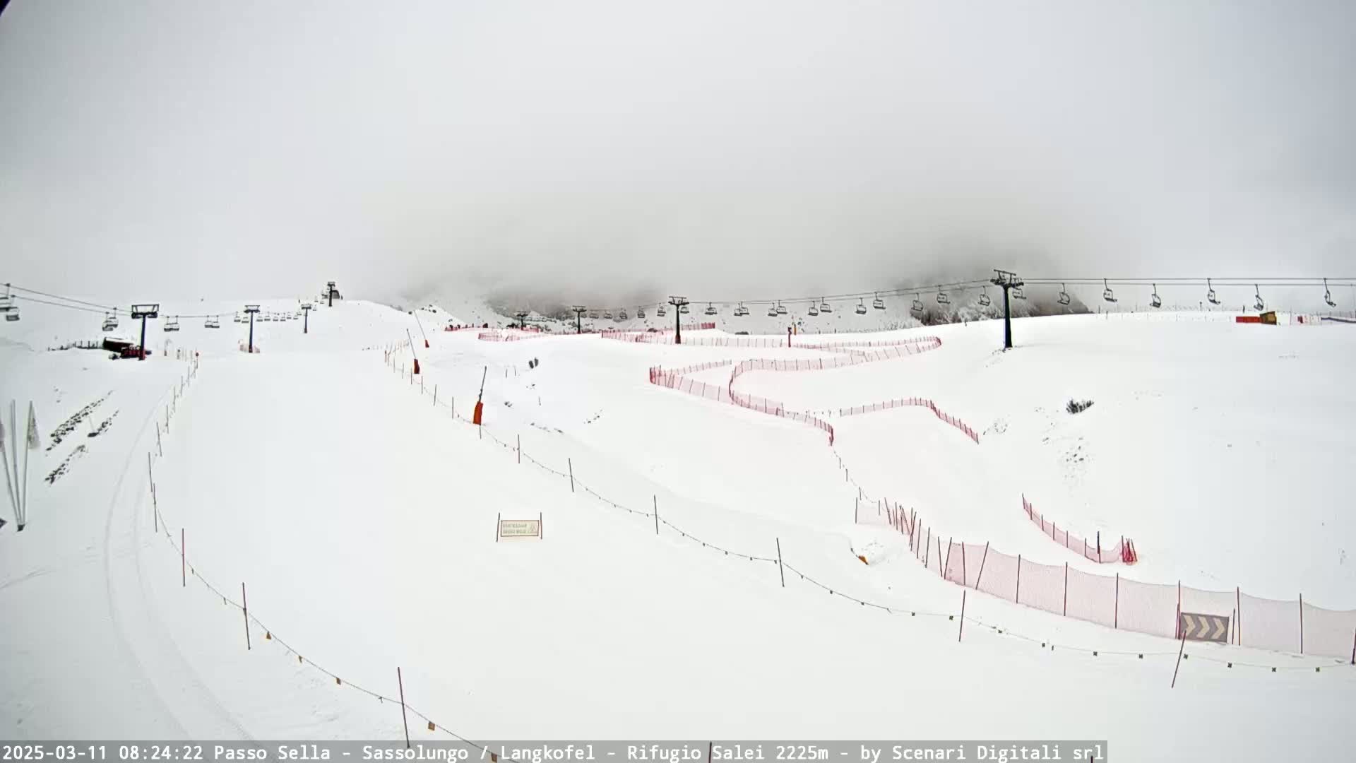 A snowy ski slope with chairlifts and red safety netting is visible under an overcast sky.