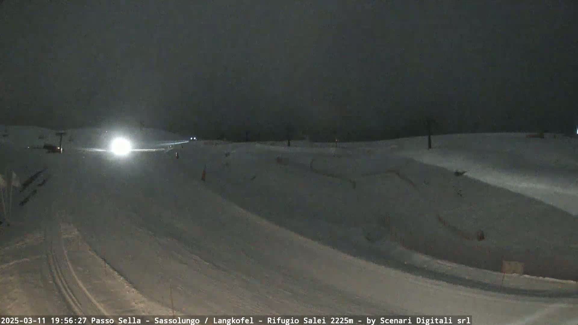 A snow-covered slope at night is illuminated by a vehicle's headlights.