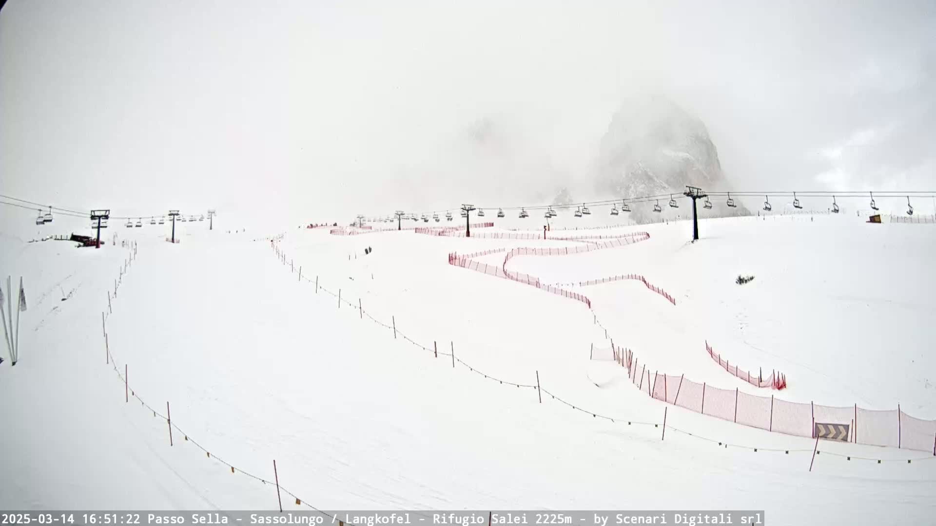 A snow-covered ski slope with chairlifts and red safety nets is visible in foggy conditions.
