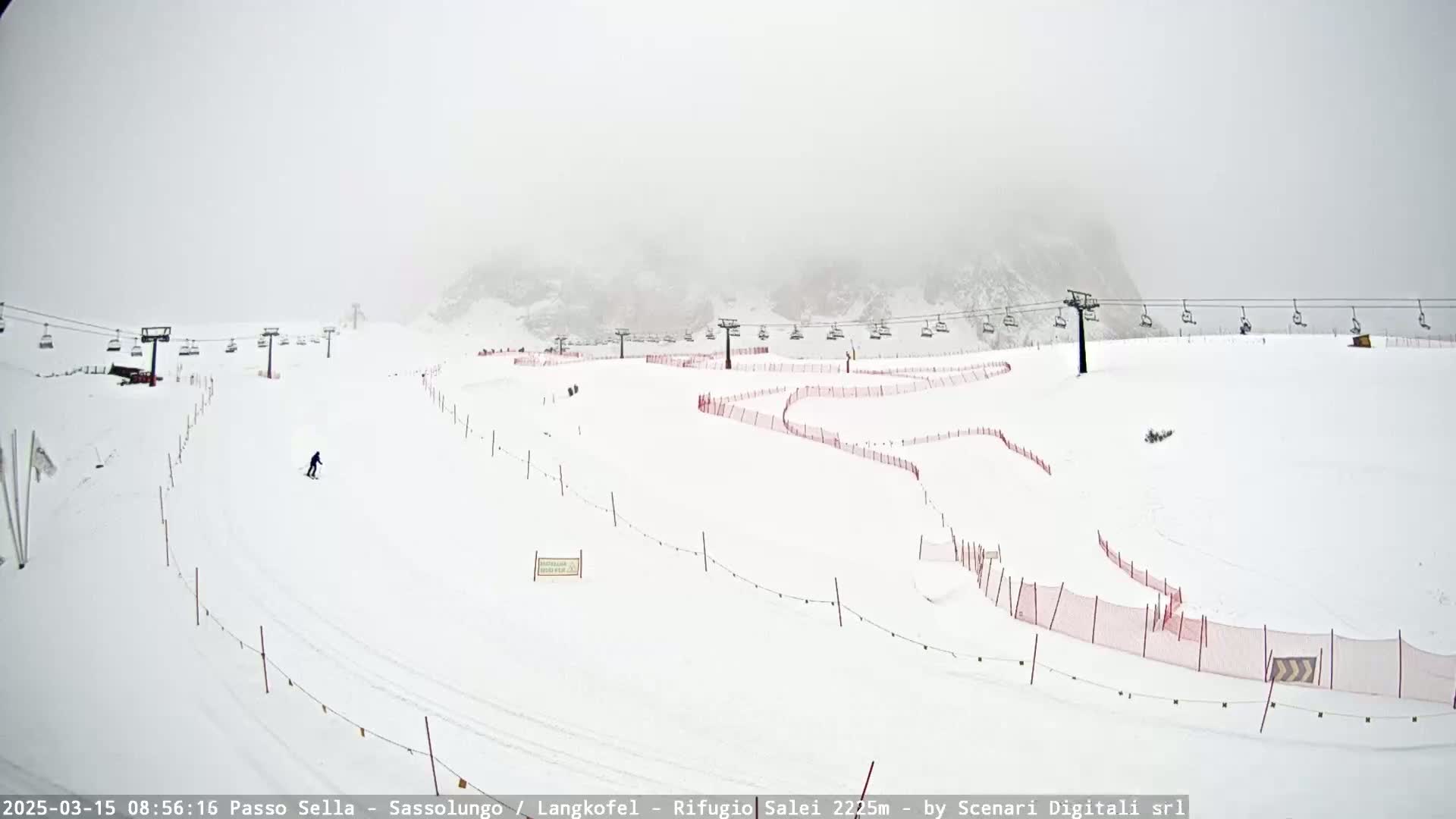 A snowy ski slope with several chairlifts and red safety nets is visible in foggy conditions.
