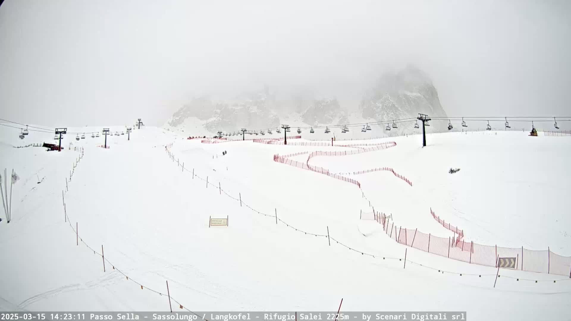A snow-covered ski slope with chairlifts and red safety nets is visible under foggy conditions.