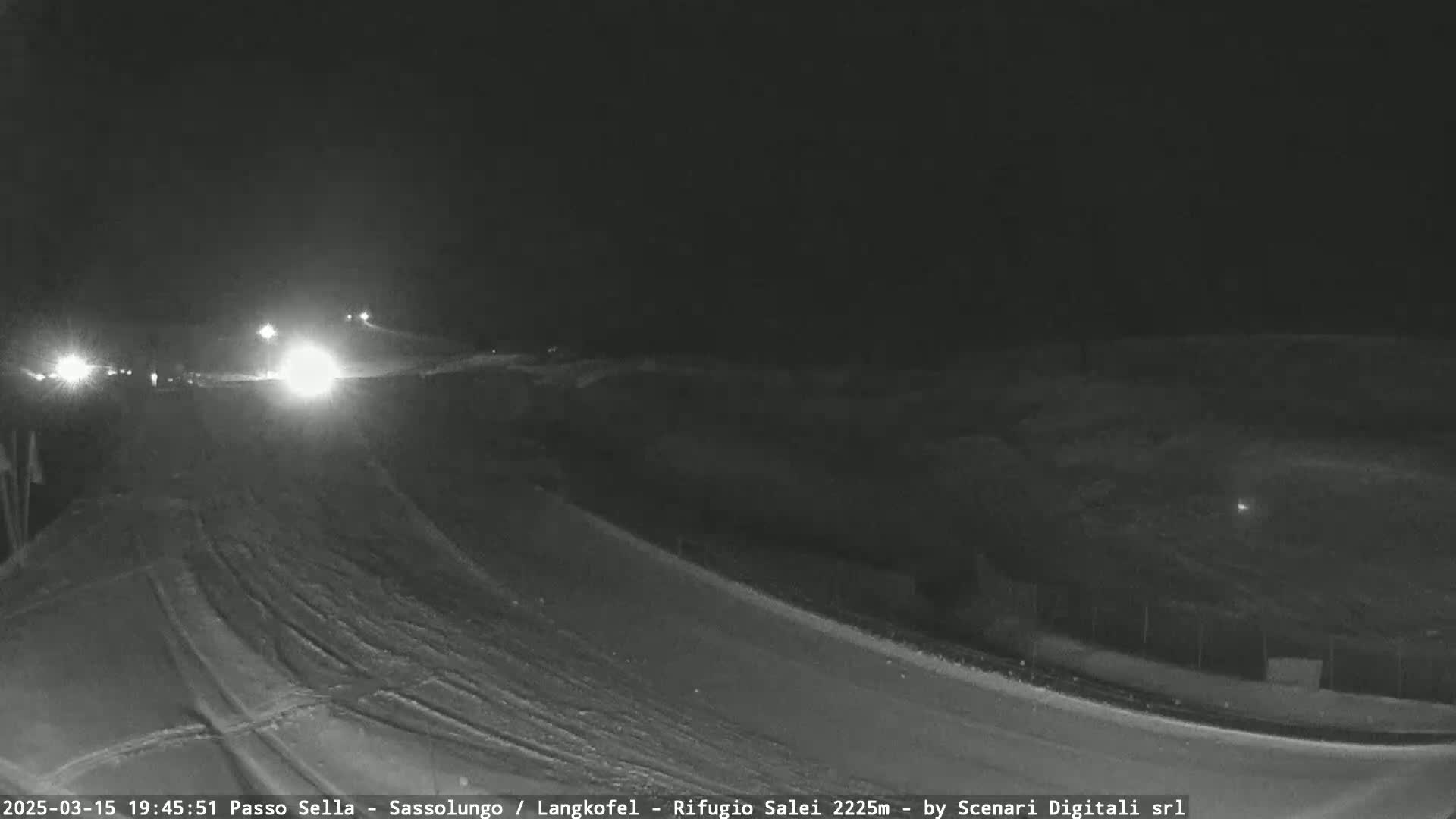 A nighttime, snow-covered road with a few vehicles driving on it is visible, with dark hills in the background.
