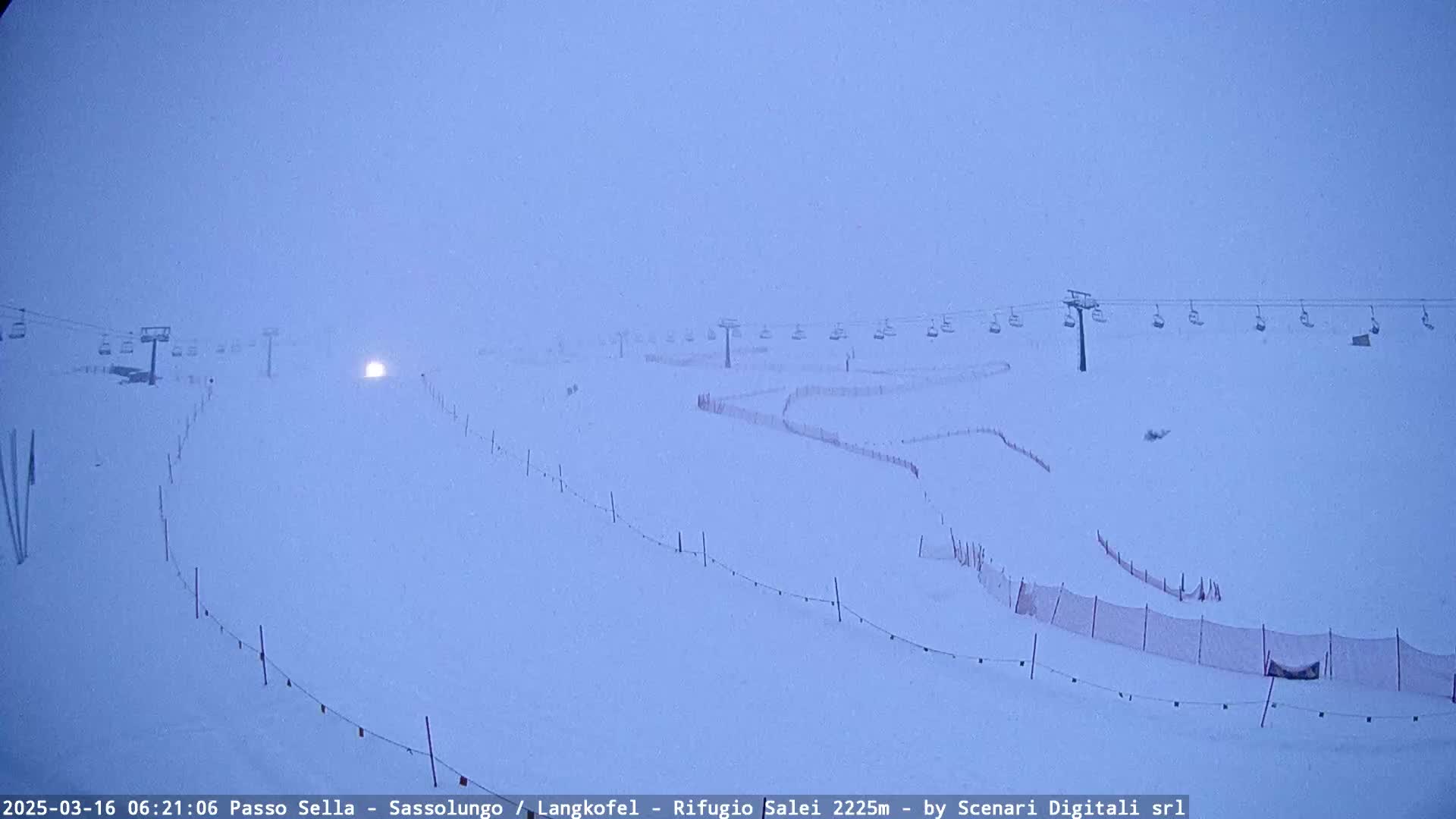 A snow-covered ski slope with chairlifts and safety netting is visible in a heavy snowstorm.