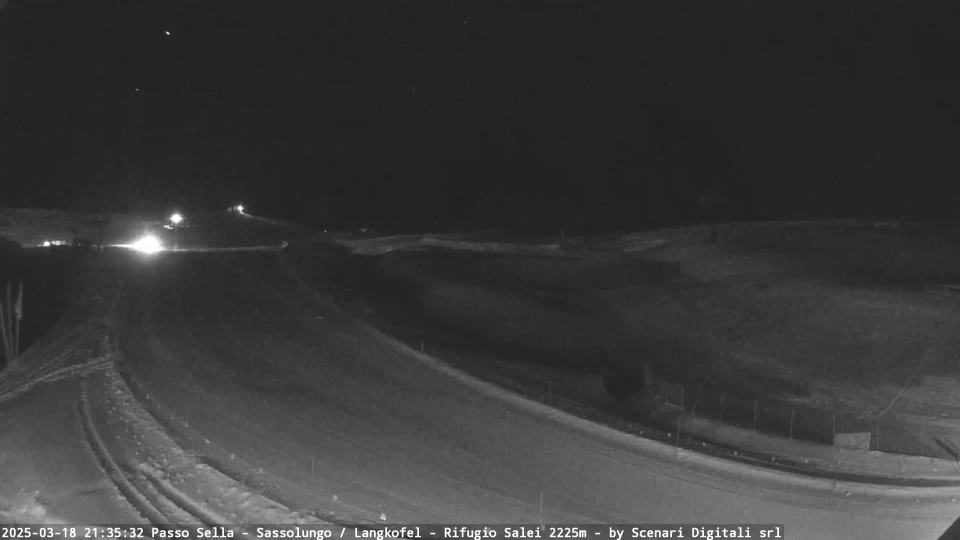 A nighttime, snow-covered road curves gently around a dark field under a clear sky.