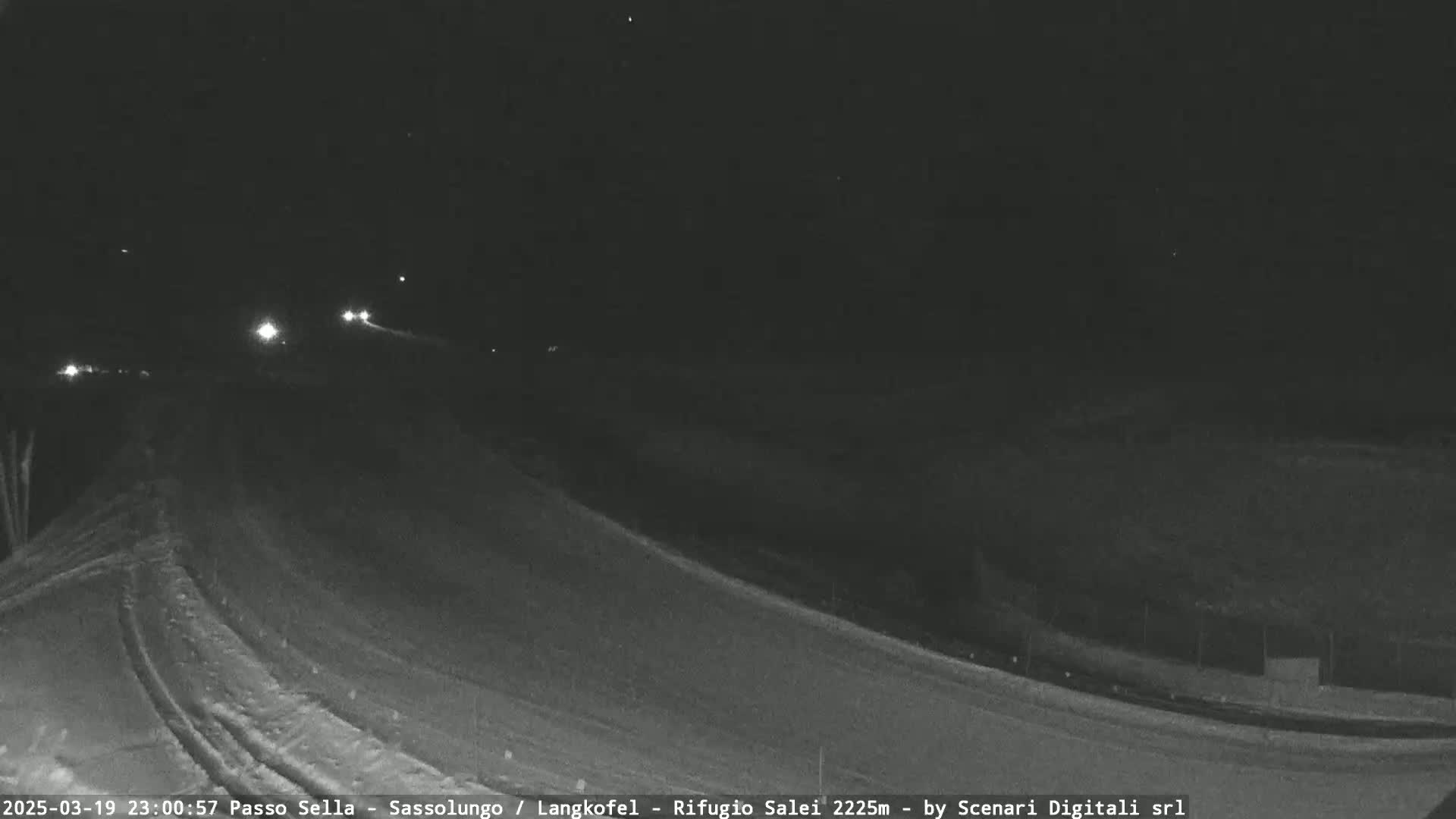 A nighttime, snowy road scene shows a few sets of vehicle headlights in the distance.