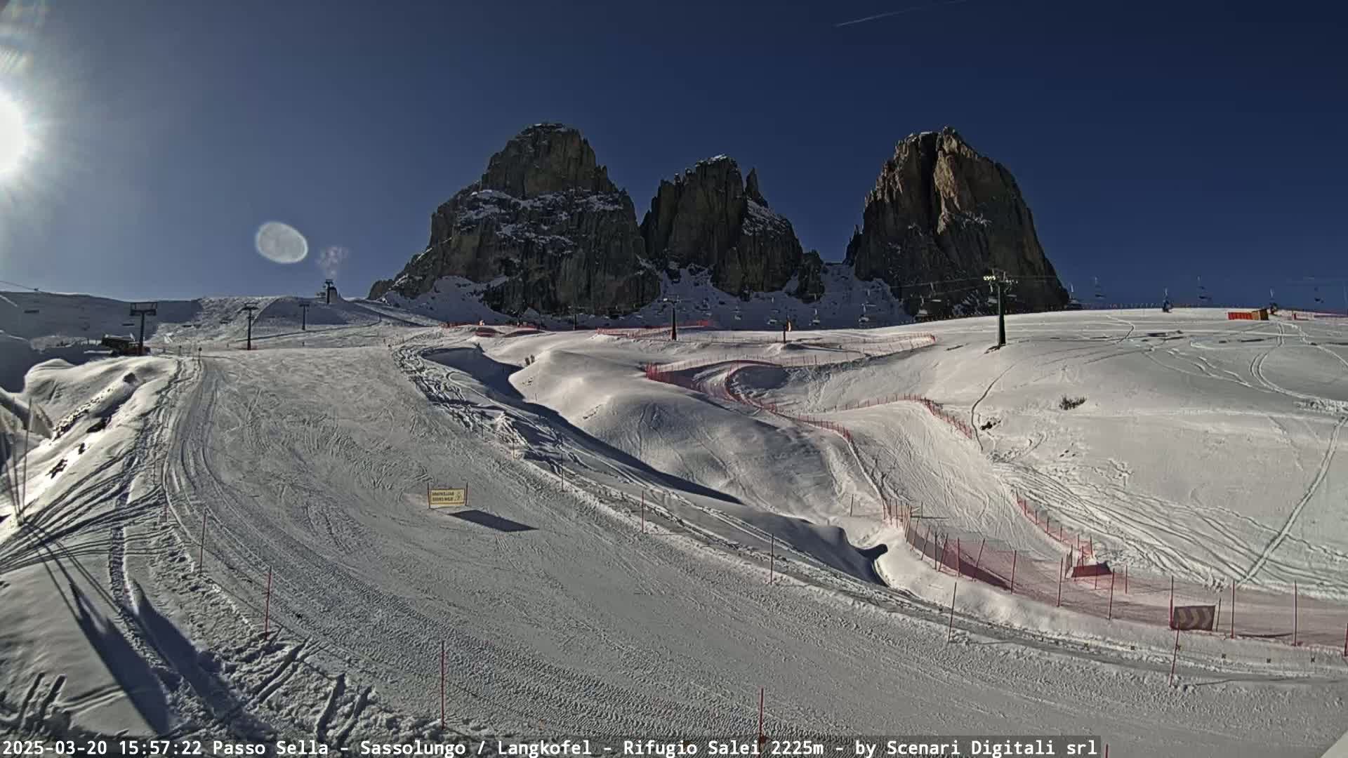 A sunny, snow-covered ski slope with several ski runs and lifts, set against a backdrop of rocky mountains.