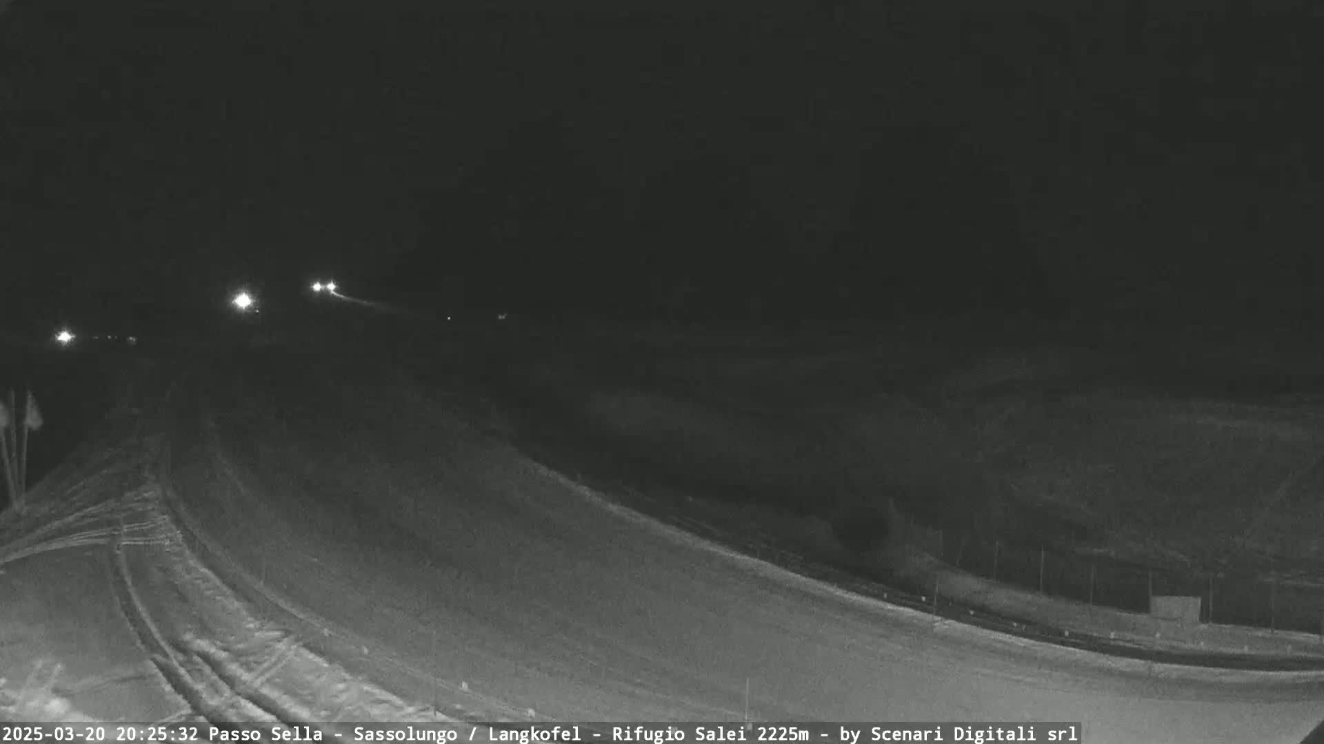 A nighttime, snow-covered road curves gently to the right, with a few vehicle headlights visible in the distance.