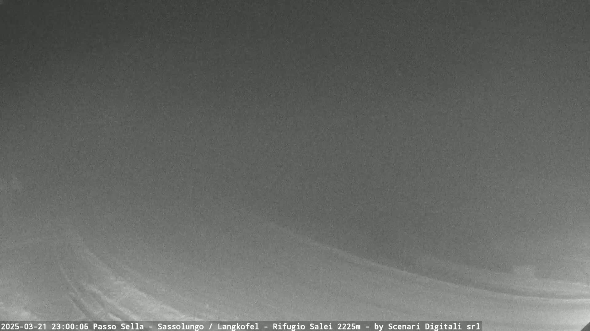 A nighttime, low-visibility view of a snow-covered road curving gently into the distance under a dark, overcast sky.