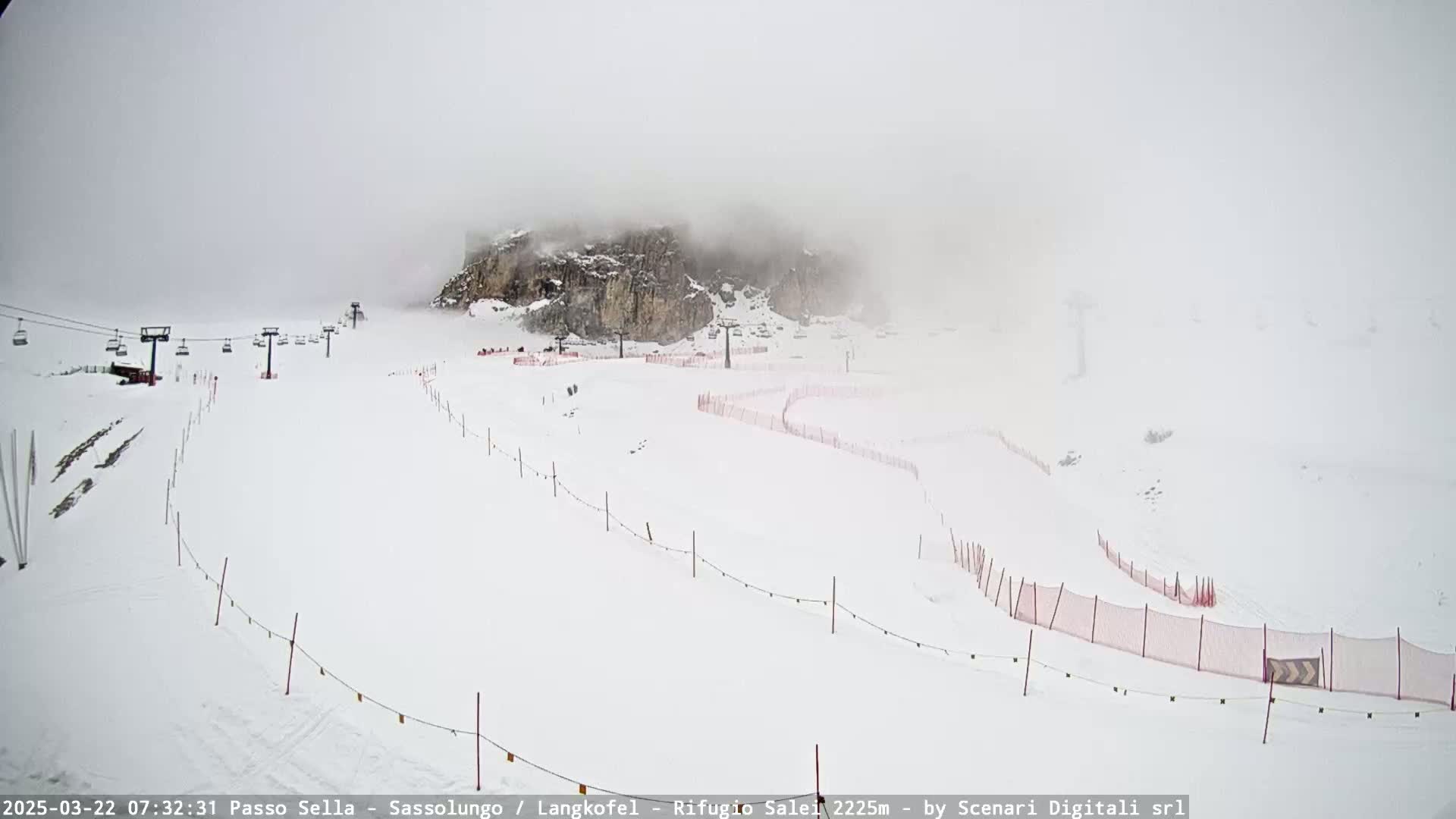 A snowy ski slope with a chairlift and fog obscuring a rocky mountain in the background.