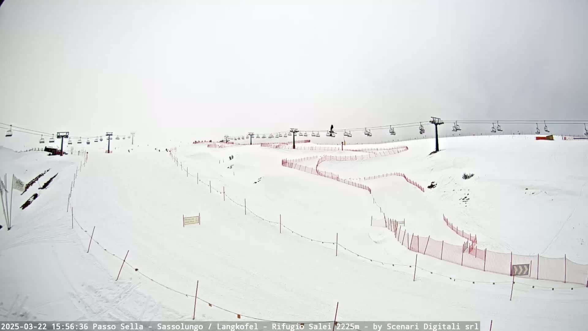 A snowy ski slope with chairlifts and red safety nets under an overcast sky.