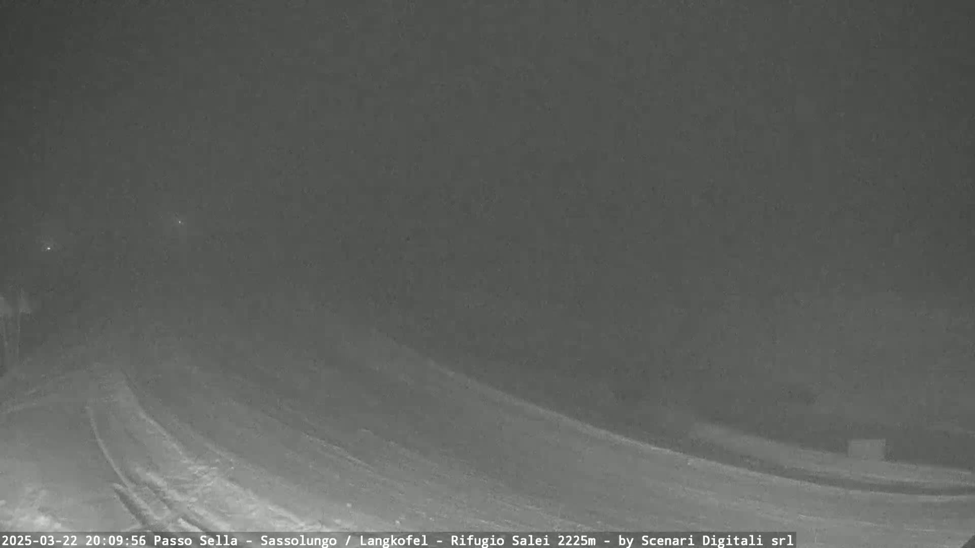 A nighttime, snow-covered road curves gently to the right under a dark sky.
