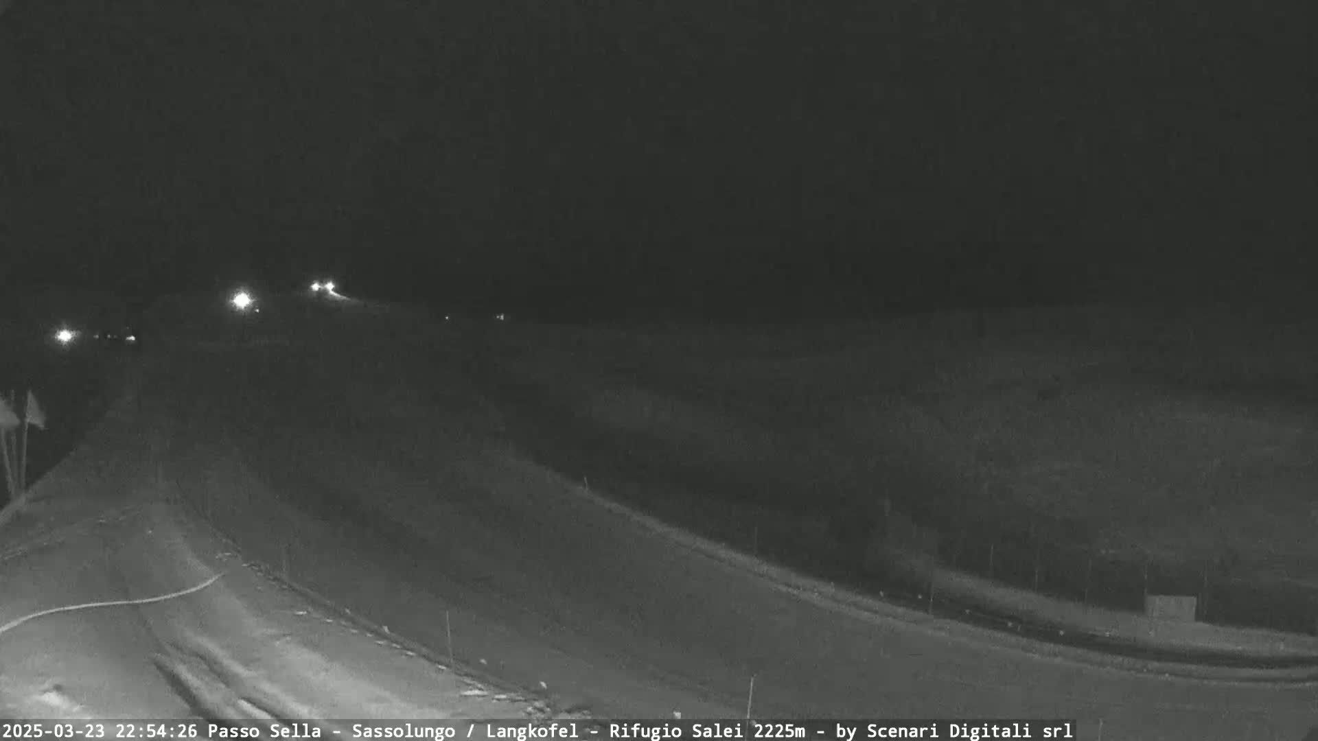 A nighttime, low-light view of a mostly empty highway curving to the right, with a few distant headlights visible.