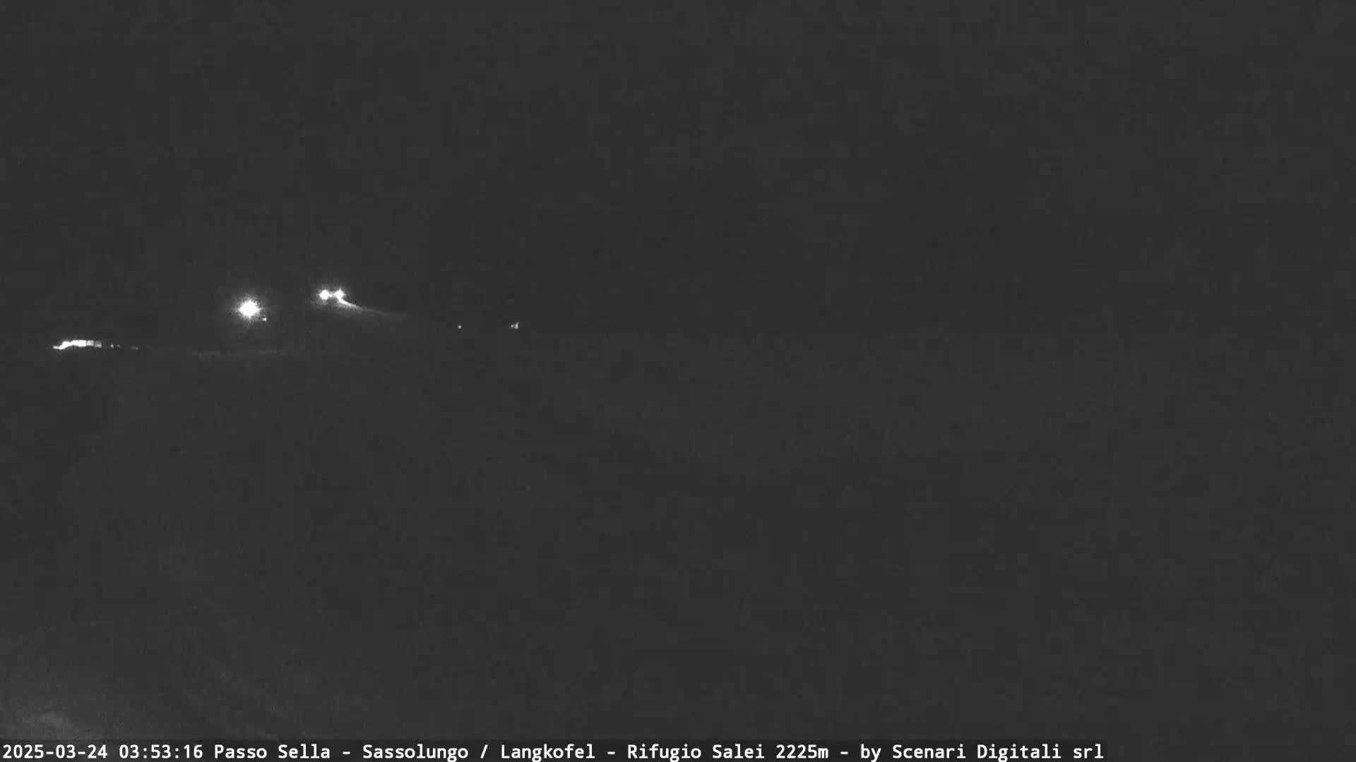 A nighttime, low-light view shows a few distant headlights on a dark road or path.