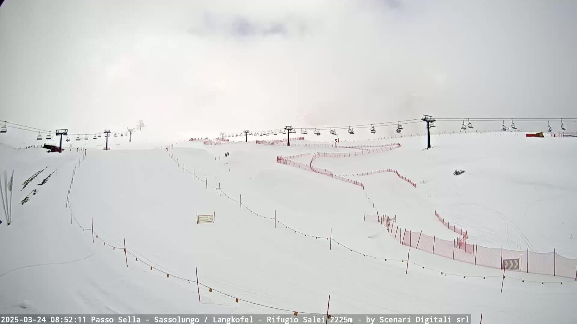 A snow-covered ski slope with chairlifts and red safety netting is visible under an overcast sky.