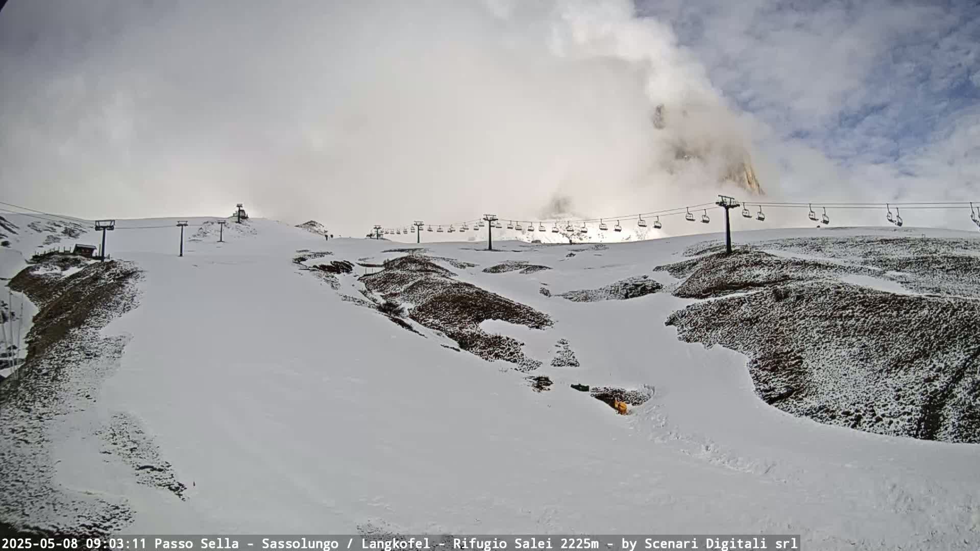 A snow-covered mountain slope with a chairlift and partly cloudy skies.