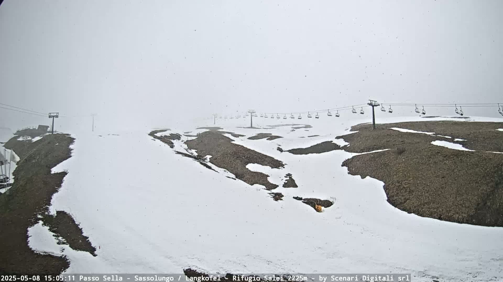 A snowy, foggy landscape features a chairlift and patches of exposed ground.