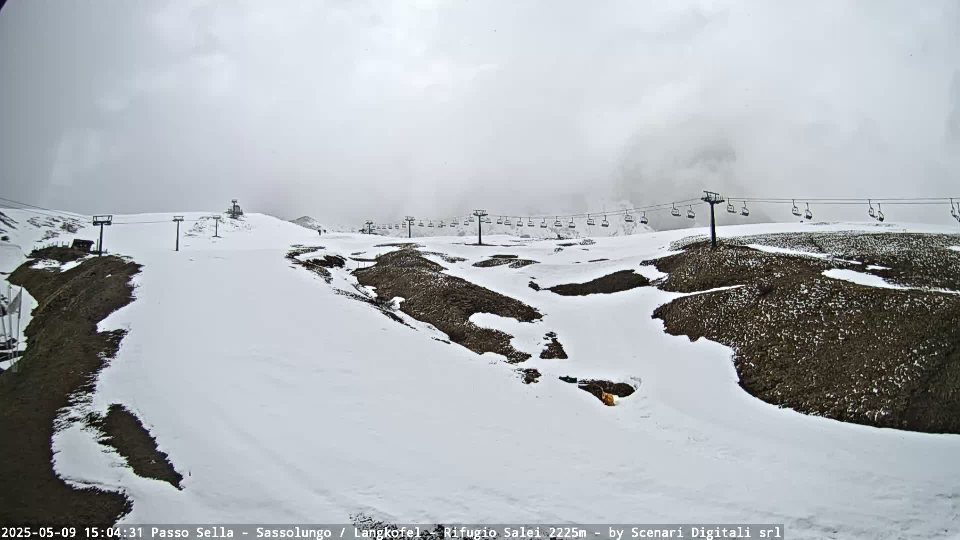 A mostly cloudy day shows a snow-covered ski slope with a chairlift running across it.