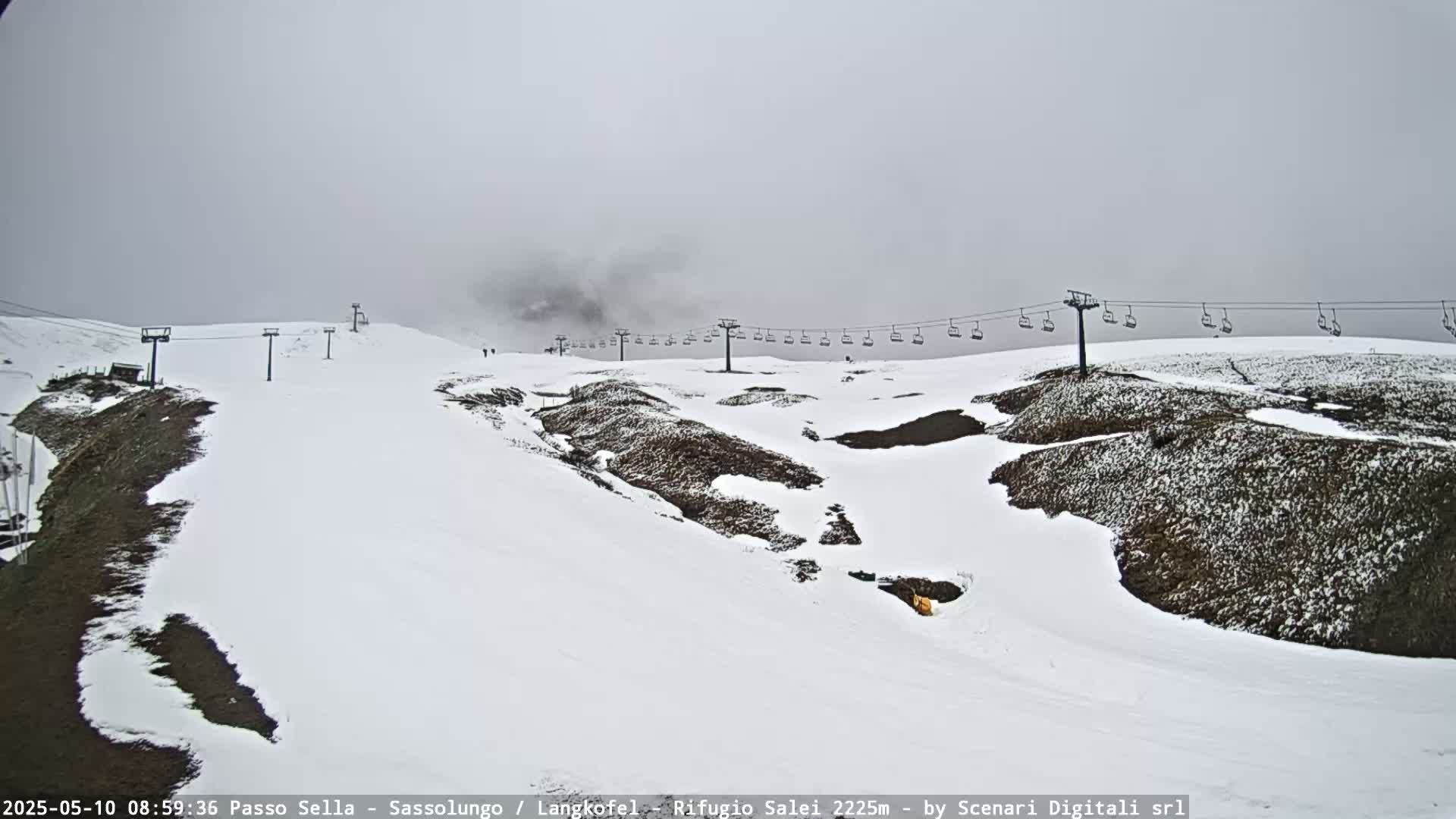 A snow-covered ski slope with a chairlift extends across a foggy, overcast mountainside.
