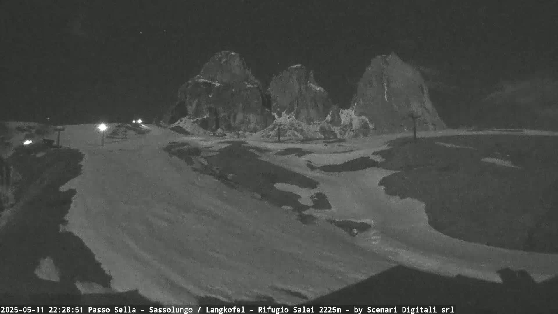 A nighttime, snow-covered landscape with several large rock formations in the background is illuminated by a few lights.