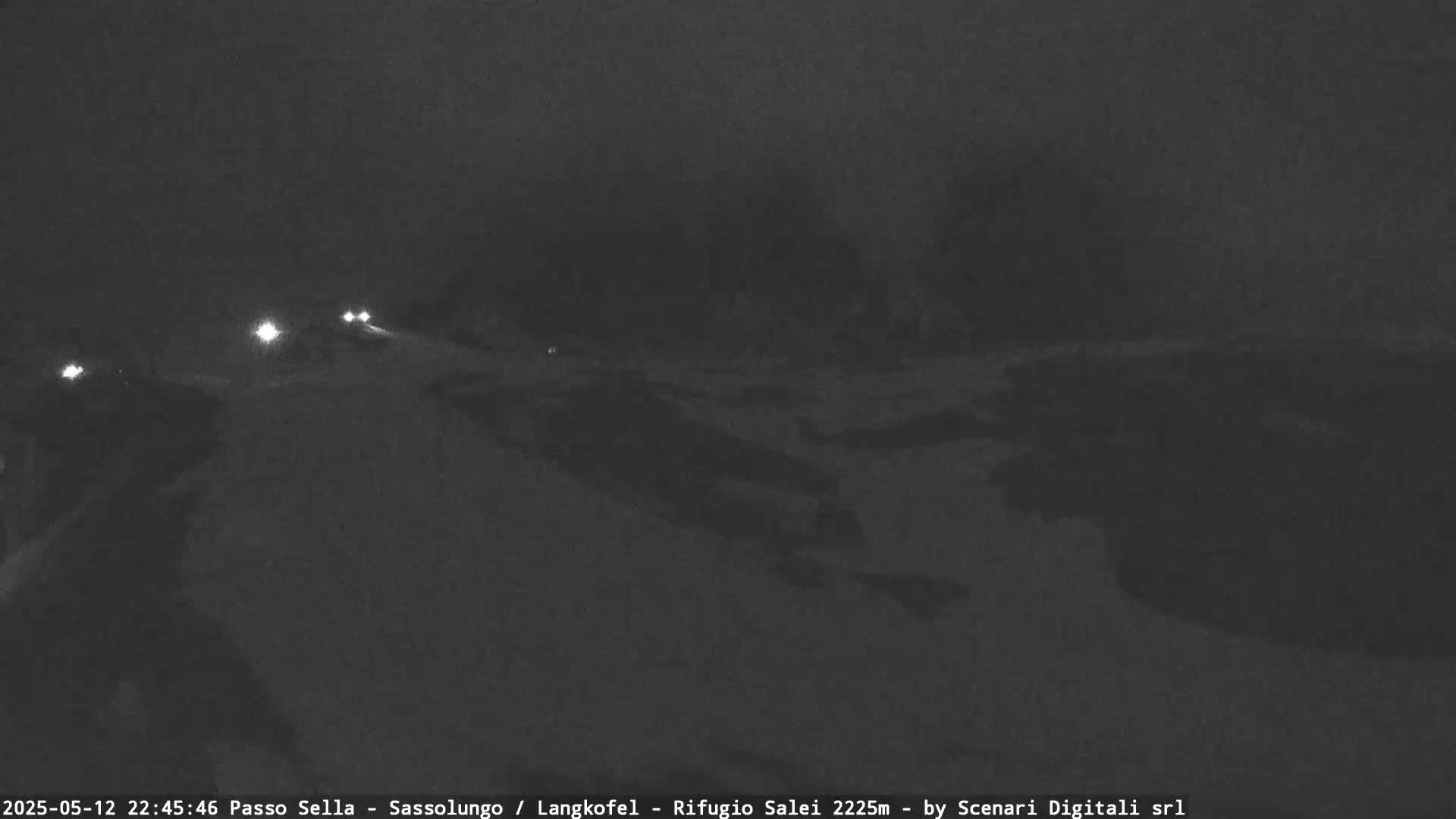 A nighttime, snowy road scene shows a few vehicles with headlights traveling away from the camera.