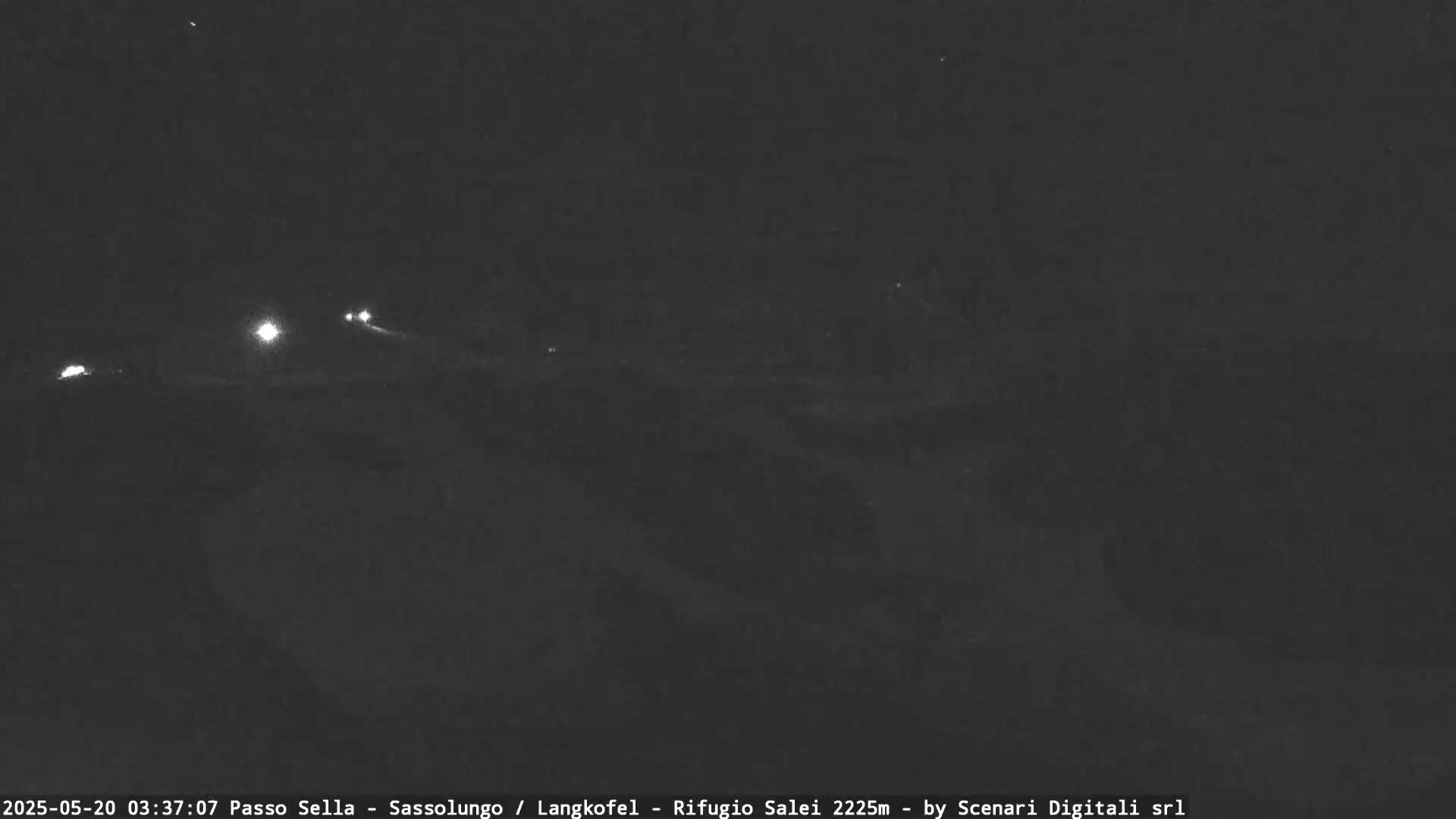 A nighttime, dark, and blurry outdoor scene shows a few distant vehicle headlights on a road.