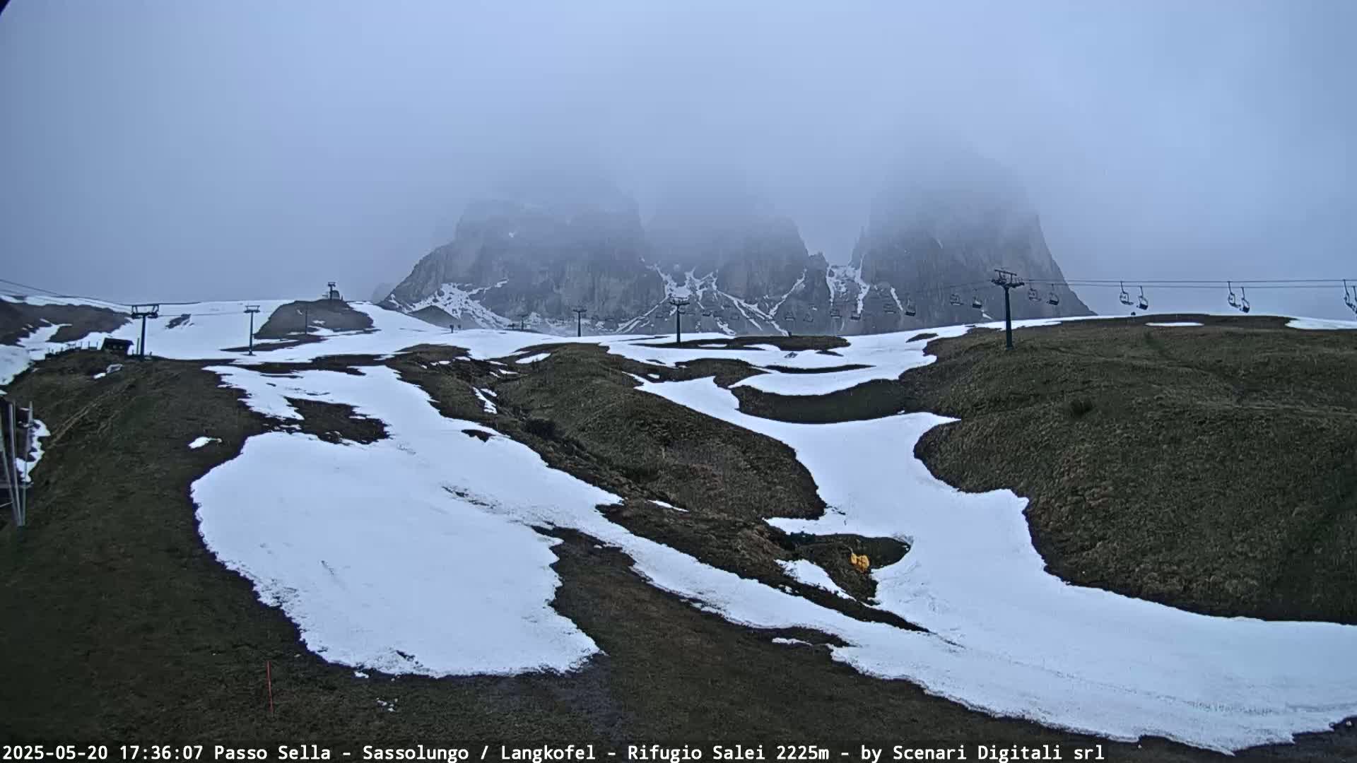 A foggy mountain landscape with patches of snow on the ground and a chairlift visible in the distance.