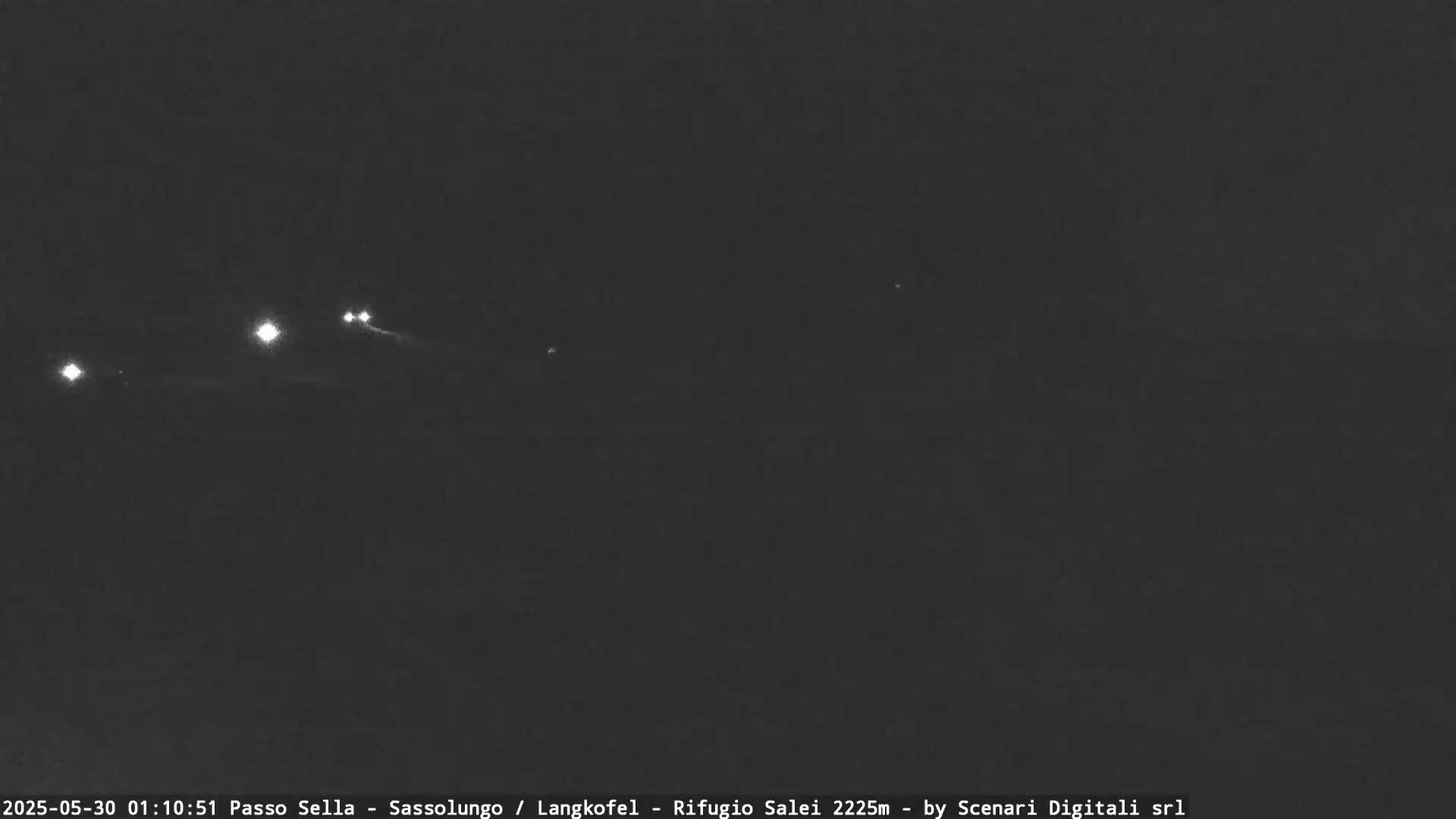 A nighttime, dark view of a road with a few distant headlights visible.