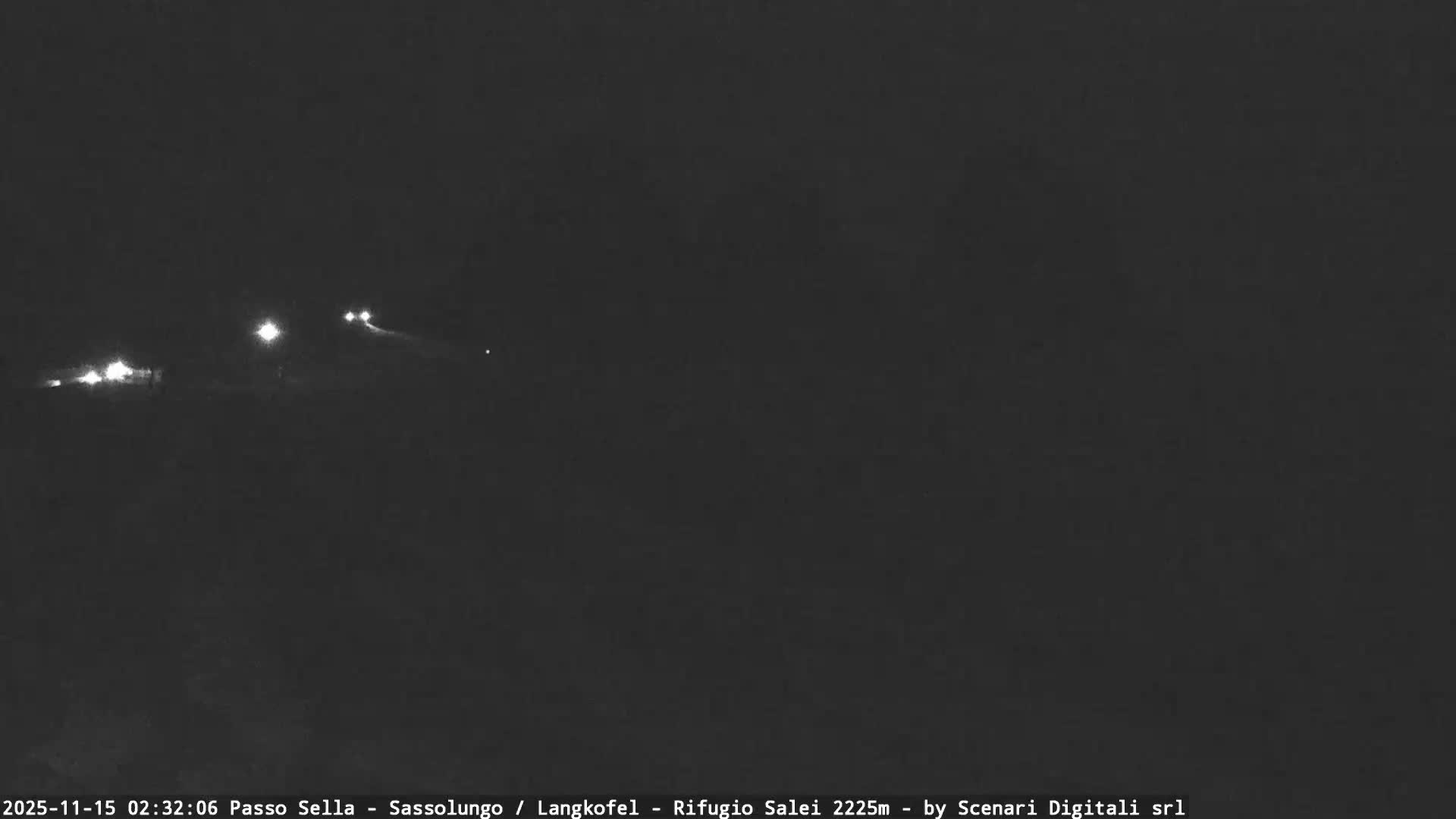 A very dark outdoor scene at night shows several diffused bright lights, likely from vehicles on a winding road, indicating low visibility due to fog or mist.