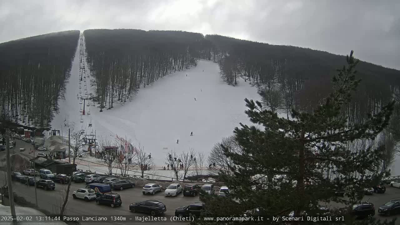 A ski slope with a chairlift and several skiers is visible on a snow-covered hillside under an overcast sky.