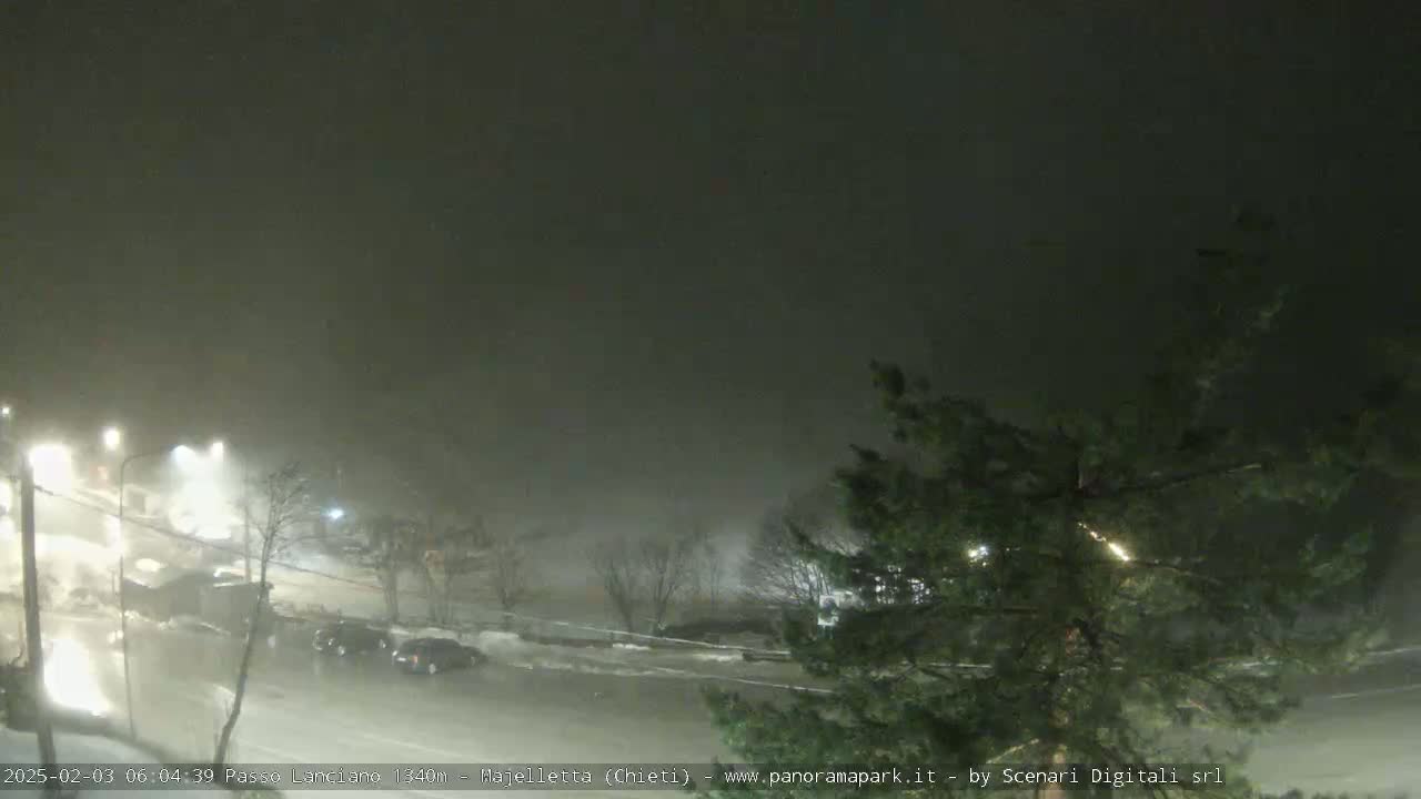A nighttime scene of a snow-covered road with sparse traffic under heavy snowfall.