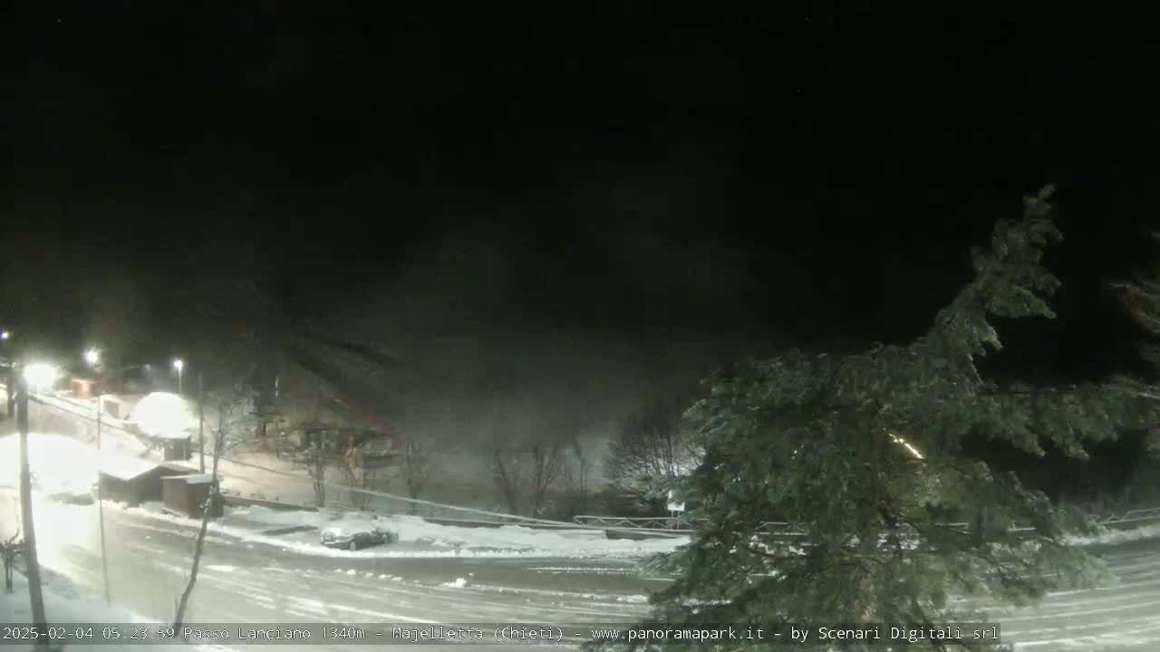 A nighttime, snow-covered parking lot and roadway are visible under a dark, possibly foggy sky.