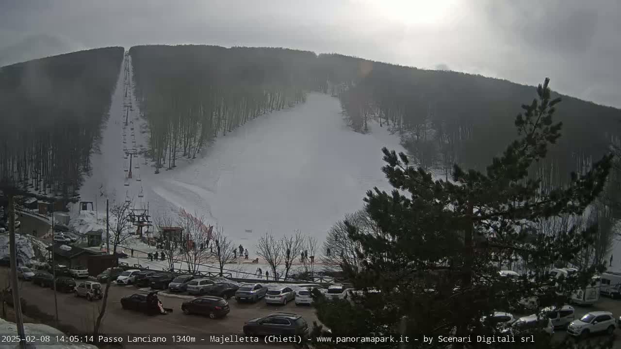 A ski slope with a chairlift, a parking lot full of cars, and a few people skiing on a somewhat hazy, sunny day.