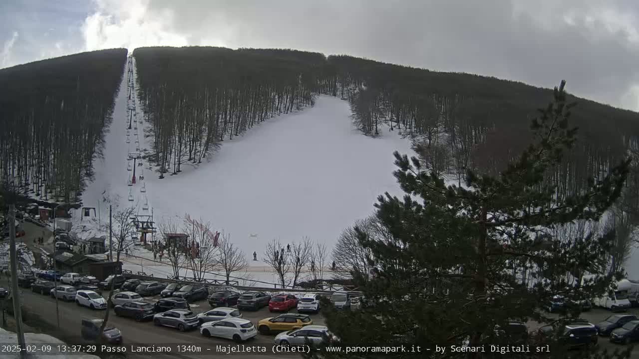 A snow-covered ski slope with a chairlift and a parking lot full of cars is visible under an overcast sky.