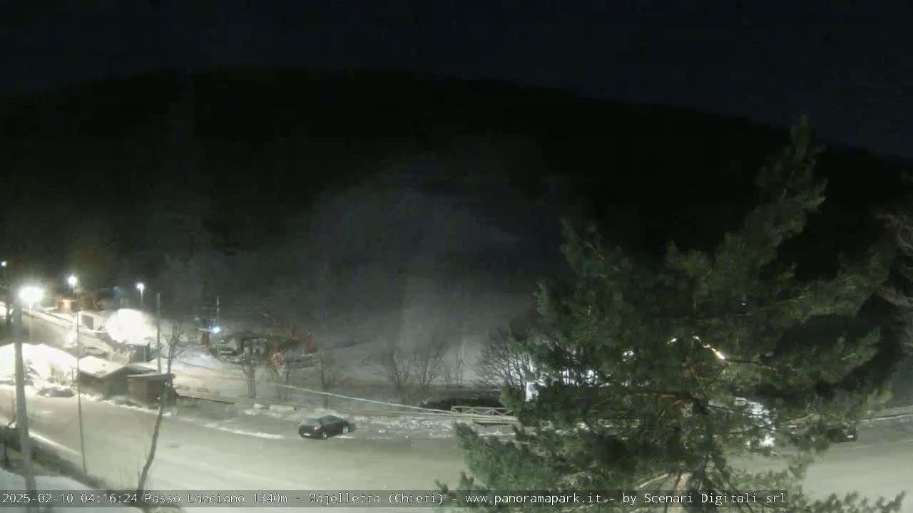 A snow-covered parking lot and roadway are visible at night, with a dark mountainside in the background under a clear sky.