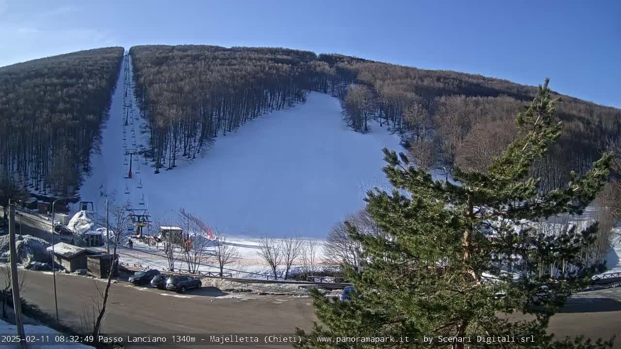 A snow-covered ski slope with a chairlift is visible on a sunny day, surrounded by a snow dusted forest.